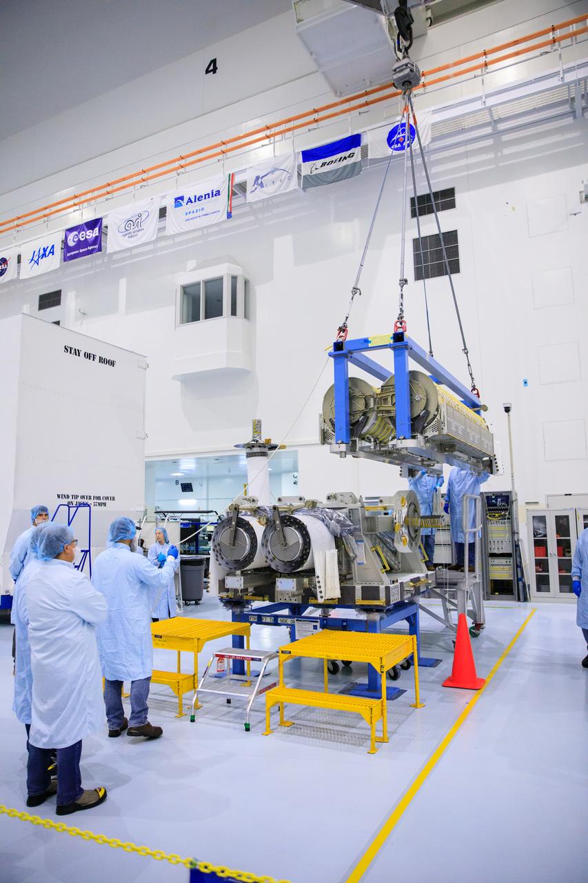 Inside the Space Station Processing Facility high bay at NASA's Kennedy Space Center in Florida, technicians monitor the progress as a crane is used to lift and stack the third set of two International Space Station Roll Out Solar Arrays (iROSA) onto a platform on March 23, 2023. They are being prepared for delivery to the space station aboard SpaceX’s Dragon cargo carrier on the company’s 28th commercial resupply services (CRS-28) mission to the space station. iROSA is a new type of solar panel that rolls open in space and is more compact than current rigid panel designs.