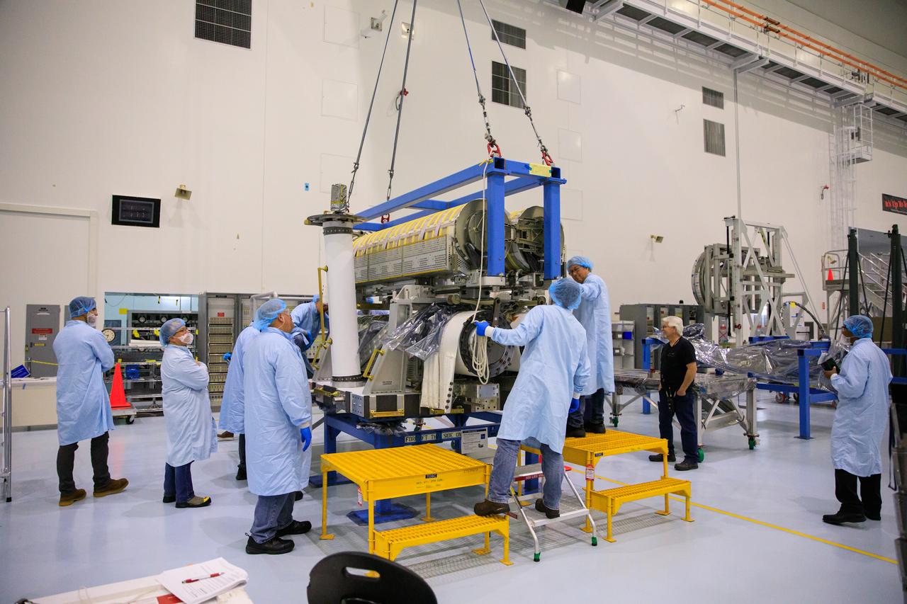 Inside the Space Station Processing Facility high bay at NASA's Kennedy Space Center in Florida, technicians assist as a crane is used to lower a set of International Space Station Roll Out Solar Arrays (iROSA) onto a platform on March 23, 2023. They are being prepared for delivery to the space station aboard SpaceX’s Dragon cargo carrier on the company’s 28th commercial resupply services (CRS-28) mission to the space station. iROSA is a new type of solar panel that rolls open in space and is more compact than current rigid panel designs.
