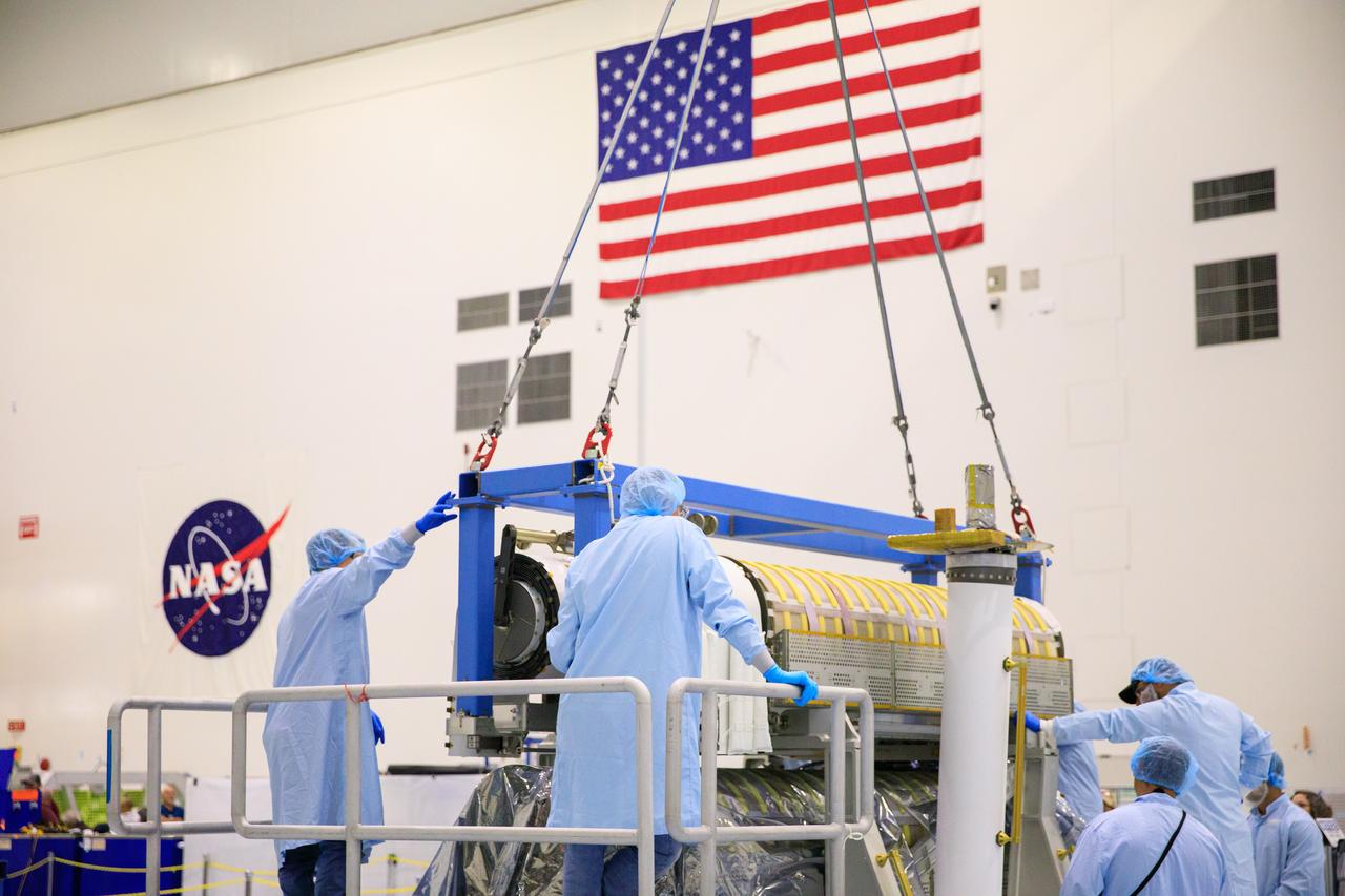 Inside the Space Station Processing Facility high bay at NASA's Kennedy Space Center in Florida, technicians assist as a crane is used to lower a set of International Space Station Roll Out Solar Arrays (iROSA) onto a platform on March 23, 2023. They are being prepared for delivery to the space station aboard SpaceX’s Dragon cargo carrier on the company’s 28th commercial resupply services (CRS-28) mission to the space station. iROSA is a new type of solar panel that rolls open in space and is more compact than current rigid panel designs.