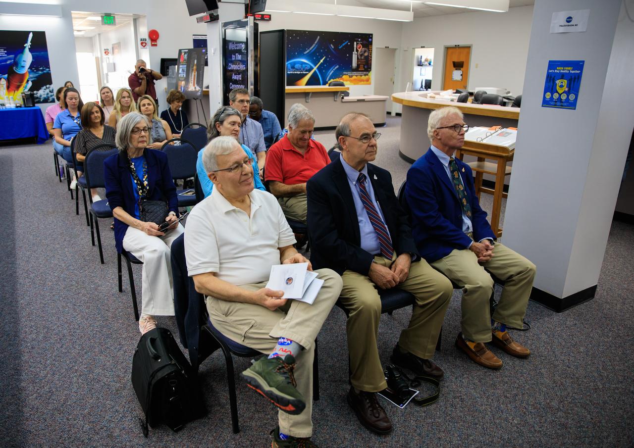 Kennedy Space Center celebrated the latest honorees to have their names added to the “Chroniclers” wall at the NASA News Center in Florida during a ceremony on May 1, 2023. Seated in front, from left are  Mark Kramer, Bob Granath, and Red Huber. They were nominated by other members of the news media and selected by a panel of NASA officials and current space reporters. The award recognizes retirees of the news and communications business who helped spread news of American space exploration from Kennedy for 10 years or more. The inductees join the list of 79 other Kennedy Chroniclers whose names hang proudly on the wall in the “Bull Pen,” the NASA News Center room where media traditionally gather to research and file their stories during launches.