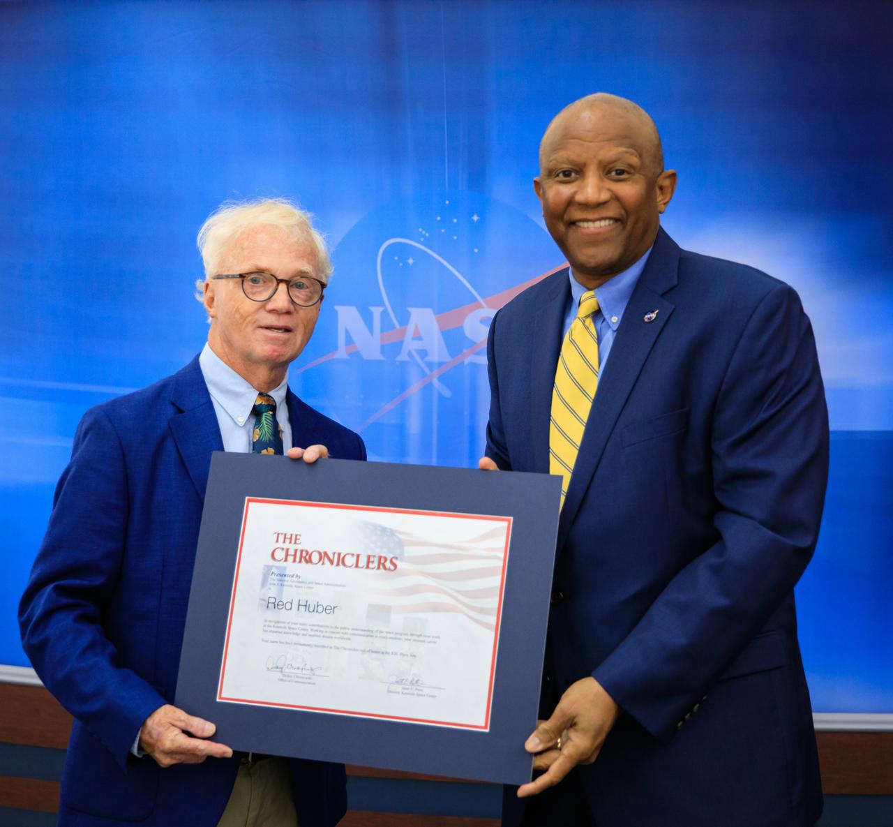 Kennedy Space Center Deputy Director Kelvin Manning, at right, presents the Chroniclers award to Red Huber during a ceremony on May 1, 2023, recognizing retired members of the news and communications business who helped spread news of American space exploration from Kennedy for 10 years or more. Kramer was honored along with Robert E. Granath and Mark Kramer  with a plaque on the “Chroniclers” wall at Kennedy’s NASA News Center in Florida. The honorees were nominated by other members of the news media and selected by a panel of NASA officials and current space reporters. They join the list of 79 other Kennedy Chroniclers whose names hang proudly on the wall in the “Bull Pen,” the NASA News Center room where media traditionally gather to research and file their stories during launches. 