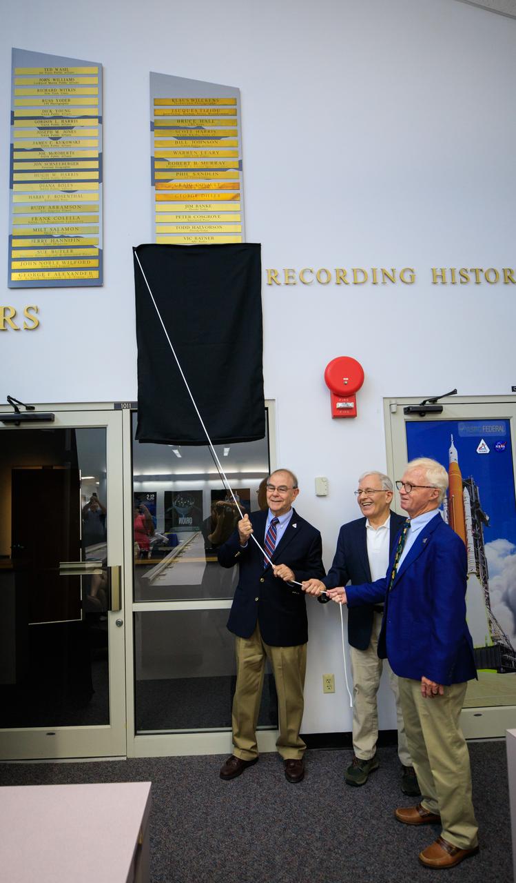 Chroniclers honorees unveil plaques bearing their names during a ceremony on May 1, 2023 at the NASA News Center at the agency’s Kennedy Space Center in Florida. From left are Robert E. Granath, Mark Kramer, and Red Huber. The trio were honored as latest members of the Chroniclers, nominated by other members of the news media and selected by a panel of NASA officials and current space reporters. The Chroniclers award recognizes retirees of the news and communications business who helped spread news of American space exploration from Kennedy for 10 years or more. The inductees join the list of 79 other Kennedy Chroniclers whose names hang proudly on the wall in the “Bull Pen,” the NASA News Center room where media traditionally gather to research and file their stories during launches. 