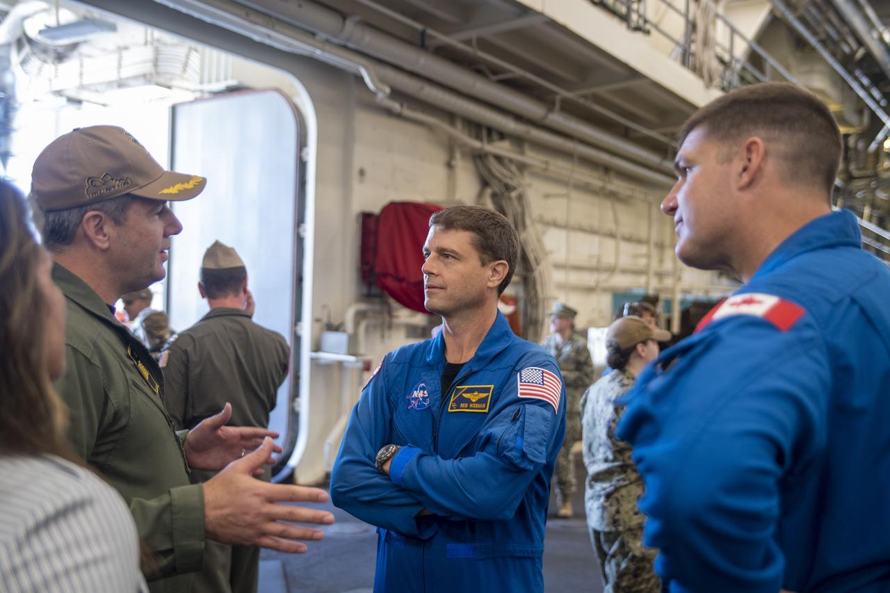 Amphibious transport dock ship USS John P. Murtha (LPD 26) Commanding Officer Capt. Doug Langenberg, left, explains to NASA Astronaut U.S. Navy Capt. Reid Wiseman and Canadian Space Agency Astronaut Jeremy Hansen, right, the ship’s recovery capabilities, July 19, 2023. In preparation for NASA's Artemis II crewed mission, which will send four astronauts in Orion beyond the Moon, NASA and the U.S. Navy will conduct a series of tests to demonstrate and evaluate the processes, procedures, and hardware used in recovery operations for crewed lunar missions. The U.S. Navy has many unique capabilities that make it an ideal partner to support NASA, including its amphibious capabilities with the ability to embark helicopters, launch and recover small boats, three-dimensional air search radar and advanced medical facilities.