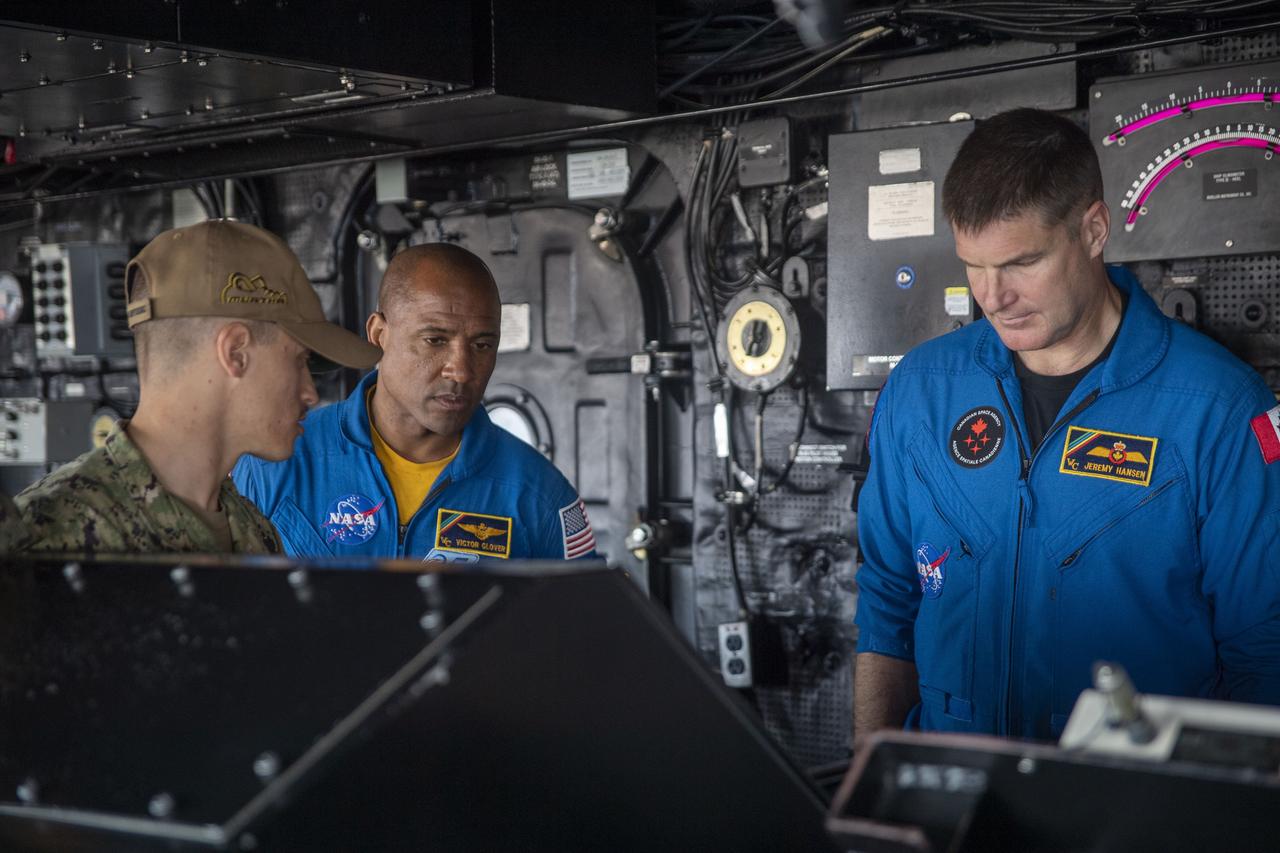 L.t. j.g Thomas Lampognana, left, explains amphibious transport dock ship USS John P. Murtha’s (LPD 26) helm control console to NASA Astronaut U.S. Navy Capt. Victor Glover and Canadian Space Agency Astronaut Jeremy Hansen, July 19, 2023. The helm is used as the primary steering for the ship underway. In preparation for NASA's Artemis II crewed mission, which will send four astronauts in Orion beyond the Moon, NASA and the U.S. Navy will conduct a series of tests to demonstrate and evaluate the processes, procedures, and hardware used in recovery operations for crewed lunar missions. The U.S. Navy has many unique capabilities that make it an ideal partner to support NASA, including its amphibious capabilities with the ability to embark helicopters, launch and recover small boats, three-dimensional air search radar and advanced medical facilities.