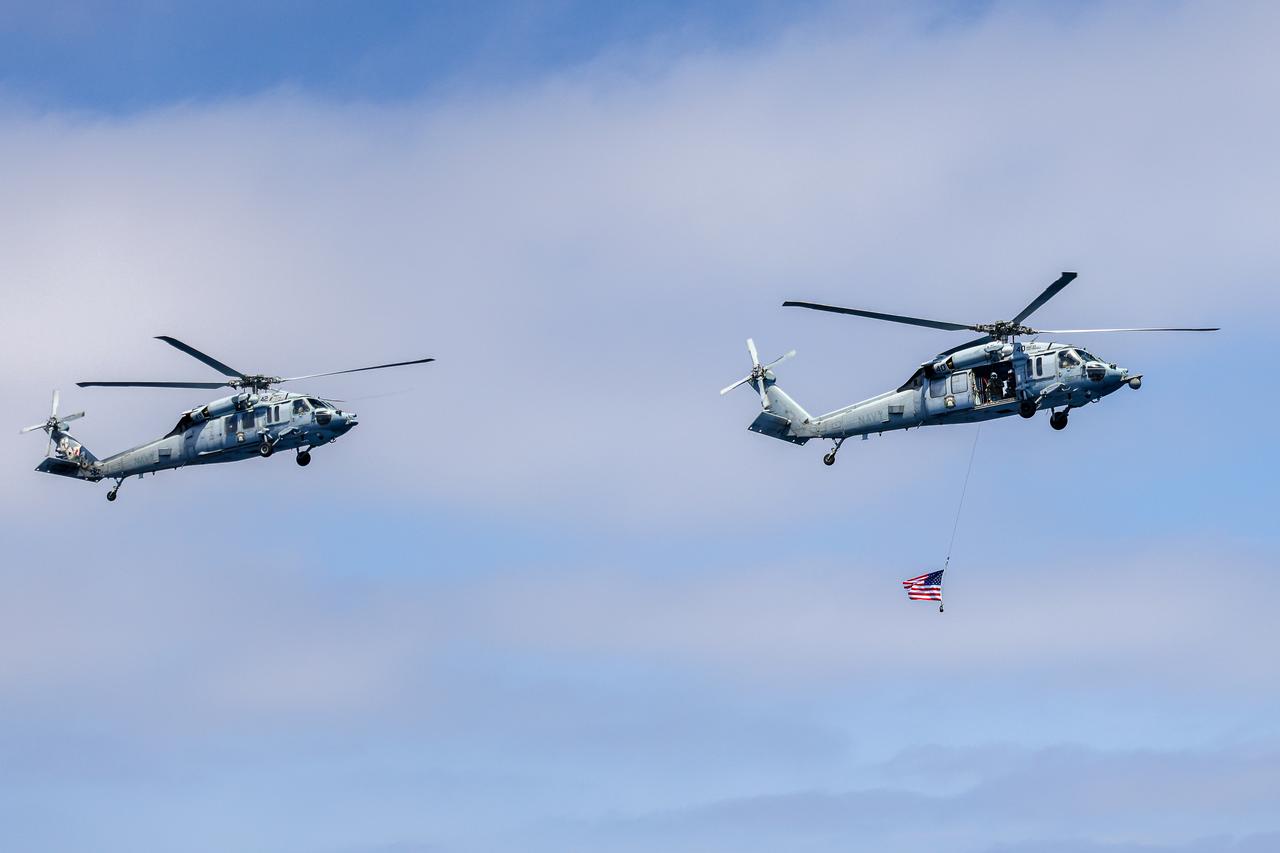 Naval helicopter pilots from Helicopter Sea Combat Squadron (HSC) 23 “Wildcards” fly over USS John P Murtha with an American flag after completing flight operations during an Artemis II mission simulation during NASA’s Underway Recovery Test 10 off the coast of San Diego.