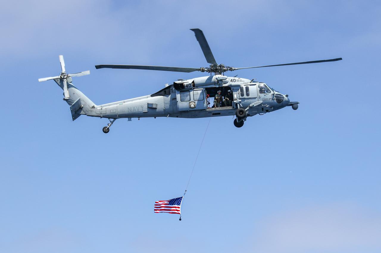 Naval helicopter pilots from Helicopter Sea Combat Squadron (HSC) 23 “Wildcards” fly over USS John P Murtha with an American flag after completing flight operations during an Artemis II mission simulation during NASA’s Underway Recovery Test 10 off the coast of San Diego.