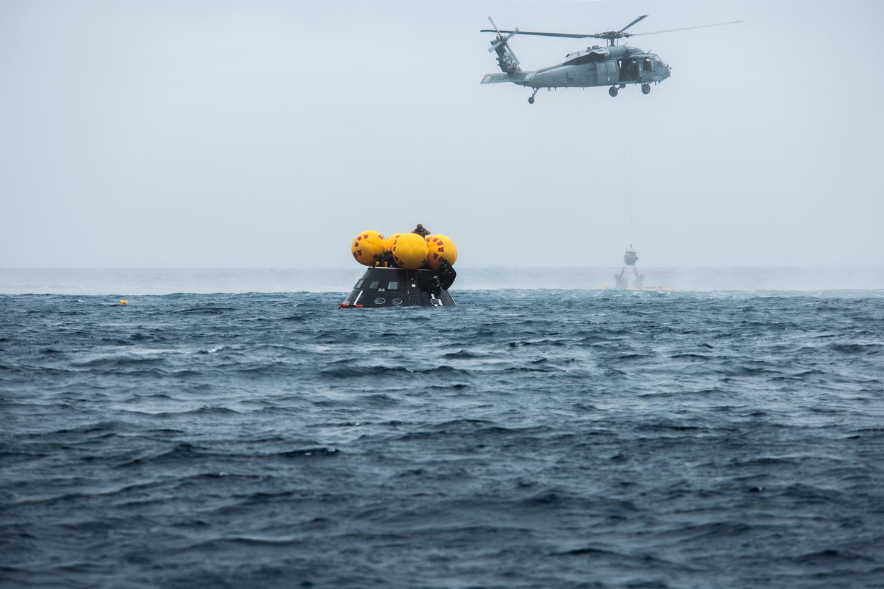 NASA, Navy, and Air Force personnel practice Artemis recovery procedures in the Pacific Ocean as part of Underway Recovery Test-10 off the coast of San Diego. In this photo Naval helicopter pilots from Helicopter Sea Combat Squadron (HSC) 23 “Wildcards” lift a pilot in a basket from an inflatable “front porch” that allows astronauts to be recovered out of the Orion spacecraft. Navy Divers from Explosive Ordnance Disposal (EOD) Expeditionary Support Unit 1 are the first to reach the spacecraft after splashdown and will assist the astronauts in getting inside the helicopter baskets prior to be flown back to the recovery ship. 