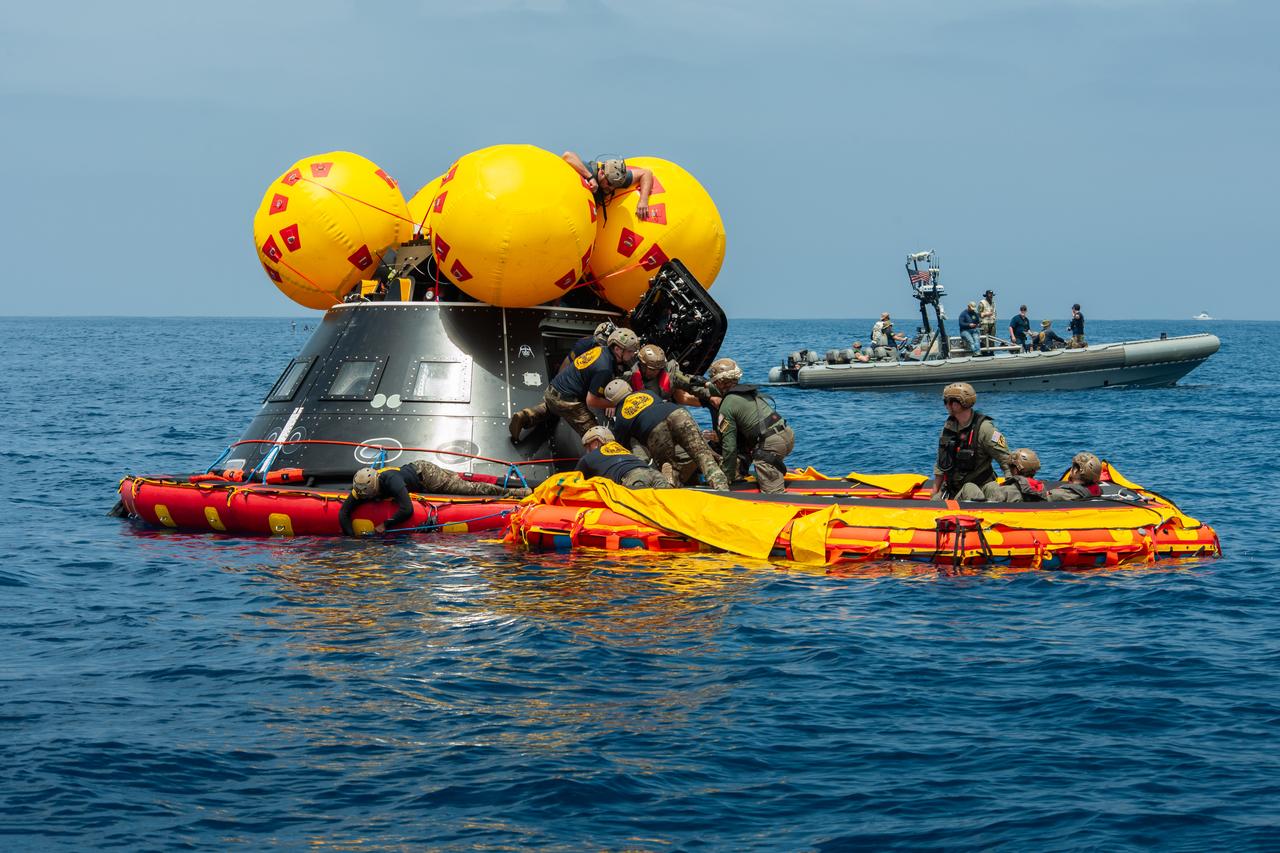 NASA, Navy, and Air Force personnel practice Artemis recovery procedures in the Pacific Ocean as part of Underway Recovery Test 10 (URT-10) off the coast of San Diego. In this photo, Navy divers are seen entering the Orion Crew Module Test Article (CMTA) and assisting a simulated crew member exiting the spacecraft to practice recovering astronauts out of the spacecraft and onto an inflatable “front porch” where the crew will be picked up with helicopters and lifted up via helicopter back to the recovery vessel.