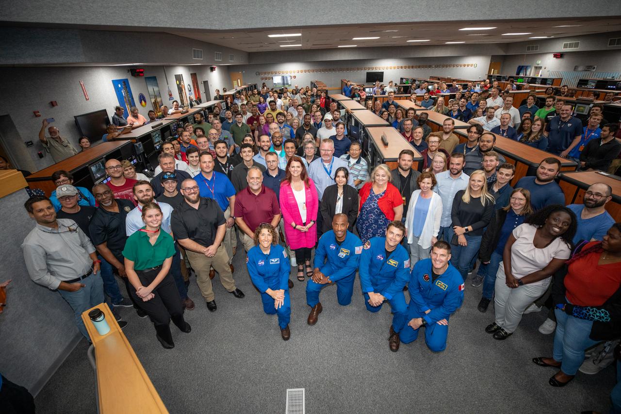 Artemis II astronauts pose for a photograph with members of the Artemis launch team inside Firing Room 1 in the Launch Control Center at NASA’s Kennedy Space Center in Florida on Aug. 7, 2023. In front, kneeling from left are NASA astronauts Christina Koch, Victor Glover, and Reid Wiseman, and CSA (Canadian Space Agency) astronaut Jeremy Hansen. The approximately 10-day Artemis II flight will test NASA’s foundational human deep space exploration capabilities, the Space Launch System rocket and Orion spacecraft, for the first time with astronauts and will pave the way for lunar surface missions, including landing the first woman and the first person of color on the Moon. 