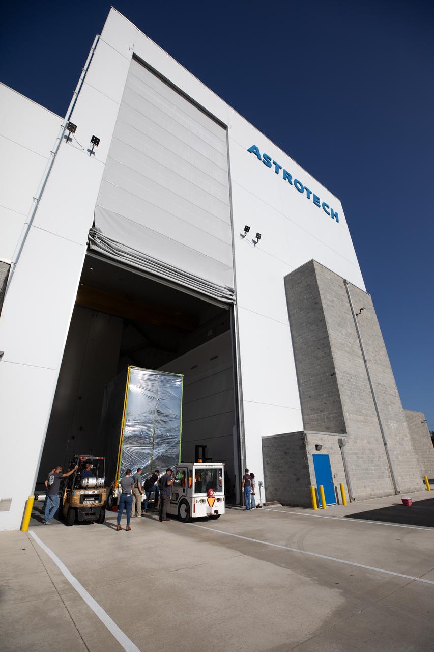 Technicians moved NASA’s Psyche spacecraft, secured for transport, into the entrance of Building 9 at the Astrotech Space Operations Facility near the agency’s Kennedy Space Center in Florida on Aug. 14, 2023. Psyche will explore its namesake, a metal-rich asteroid orbiting the Sun between Mars and Jupiter. Psyche has NASA’s Deep Space Optical Communications (DSOC) technology demonstration onboard the spacecraft. DSOC will be the agency's first demonstration of optical communication beyond the Moon. Psyche will launch atop a SpaceX Falcon Heavy rocket from Launch Complex 39A at Kennedy. Launch is targeted for Oct. 5, 2023. 
