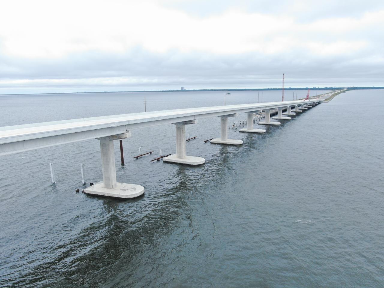In this aerial view, crews with Orion Marine Construction work to complete the westbound span of the Indian River Bridge while daily traffic moves along the upgraded eastbound lanes of the bridge leading to NASA’s Kennedy Space Center in Florida on Monday, Nov. 27, 2023. The bridge crosses the Indian River Lagoon and connects Kennedy and the Cape Canaveral Space Force Station to the mainland via State Road 405/NASA Causeway in nearby Titusville. The new high-rise bridge serves as the primary entrance and exit to the space center for employees and visitors. The new bridge spans replace a pair of two-lane drawbridges built in the mid-1960s to support NASA’s Apollo program. The first of the two new spans opened to the public ahead of schedule on June 9, 2023. In development for well over a decade, the load capacity, width, and grade of the bridge were designed to support the largest future payloads and vehicles at the spaceport while simultaneously supporting increased public traffic to and from Kennedy. 