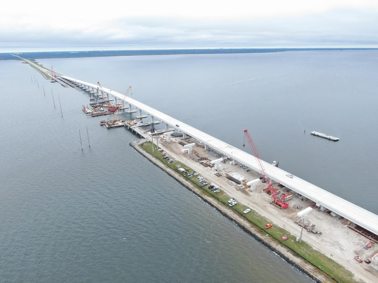 In this aerial view, crews with Orion Marine Construction work to complete the westbound span of the Indian River Bridge while daily traffic moves along the upgraded eastbound lanes of the bridge leading to NASA’s Kennedy Space Center in Florida on Monday, Nov. 27, 2023. The bridge crosses the Indian River Lagoon and connects Kennedy and the Cape Canaveral Space Force Station to the mainland via State Road 405/NASA Causeway in nearby Titusville. The new high-rise bridge serves as the primary entrance and exit to the space center for employees and visitors. The new bridge spans replace a pair of two-lane drawbridges built in the mid-1960s to support NASA’s Apollo program. The first of the two new spans opened to the public ahead of schedule on June 9, 2023. In development for well over a decade, the load capacity, width, and grade of the bridge were designed to support the largest future payloads and vehicles at the spaceport while simultaneously supporting increased public traffic to and from Kennedy. 