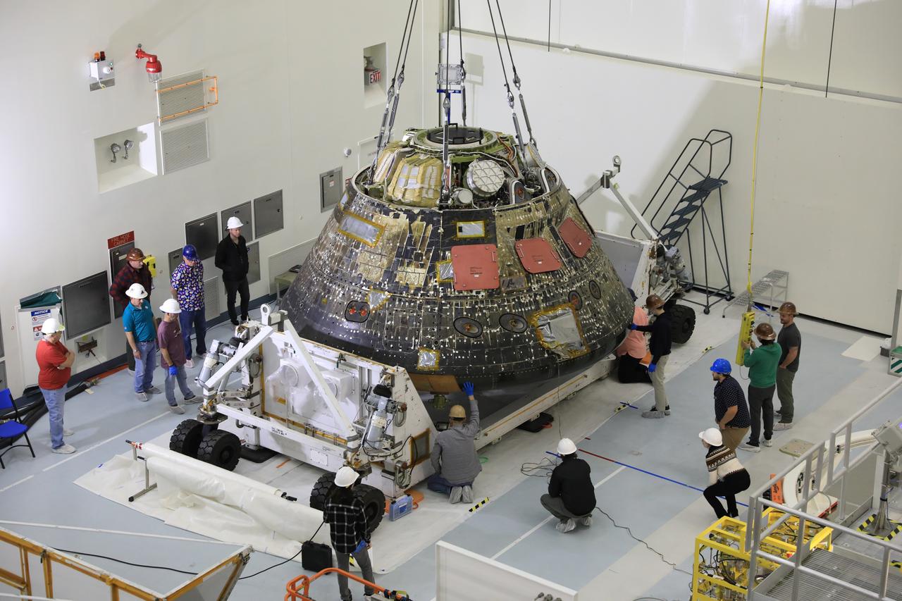 Technicians inside NASA’s Kennedy Space Centers Multi-Payload Processing Facility (MPPF) in Florida use a crane to load the Artemis I spacecraft - now called an environmental test article – into the crew module transportation fixture in preparation for its departure to NASA’s Neil Armstrong Test Facility in Sandusky, Ohio