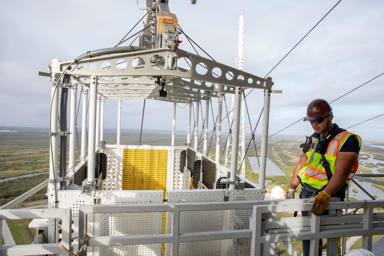 Teams with NASA’s Exploration Ground Systems Program, in preparation for the agency’s Artemis II crewed mission to the Moon, begin installing the first of four emergency egress baskets on the mobile launcher at Launch Complex 39B at the agency’s Kennedy Space Center in Florida on Wednesday, Jan. 24, 2024. The baskets, similar to gondolas on ski lifts, are used in the case of a pad abort emergency to enable astronauts and other pad personnel a way to quickly escape away from the mobile launcher to the base of the pad and where waiting emergency transport vehicles will then drive them away.