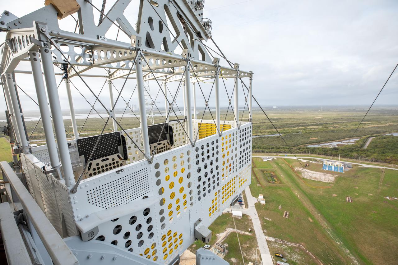 Teams with NASA’s Exploration Ground Systems Program, in preparation for the agency’s Artemis II crewed mission to the Moon, begin installing the first of four emergency egress baskets on the mobile launcher at Launch Complex 39B at the agency’s Kennedy Space Center in Florida on Wednesday, Jan. 24, 2024. The baskets, similar to gondolas on ski lifts, are used in the case of a pad abort emergency to enable astronauts and other pad personnel a way to quickly escape away from the mobile launcher to the base of the pad and where waiting emergency transport vehicles will then drive them away.