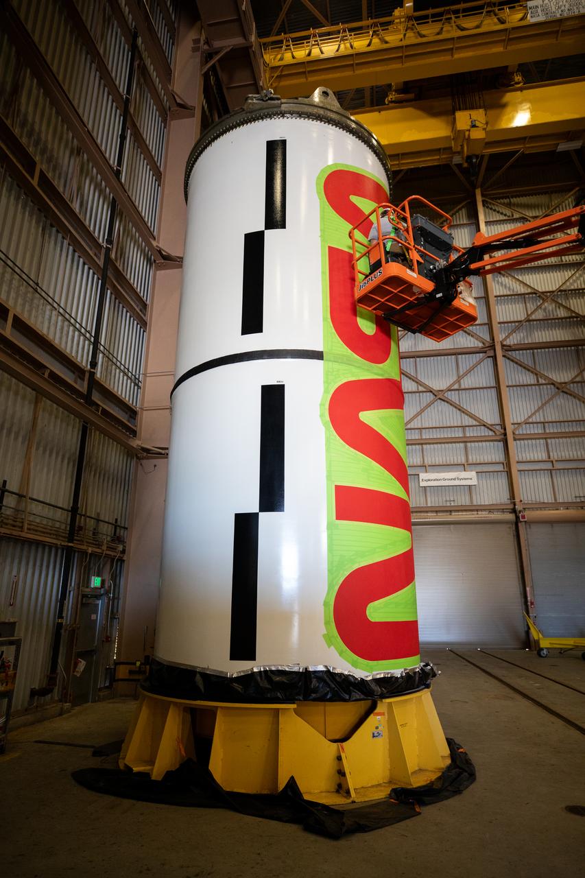 Workers with NASA’s Exploration Ground Systems (EGS) paint the bright red NASA “worm” logo on the side of an Artemis II solid rocket booster segment inside the Rotation, Processing and Surge Facility (RPSF) at Kennedy Space Center in Florida on Tuesday, Jan. 30, 2024. The EGS team used a laser projector to mask off the logo with tape, then painted the first coat of the iconic design. The booster segments will help propel the Space Launch System (SLS) rocket on the Artemis II mission to send four astronauts around the Moon as part of the agency’s effort to establish a long-term science and exploration presence at the Moon, and eventually Mars.