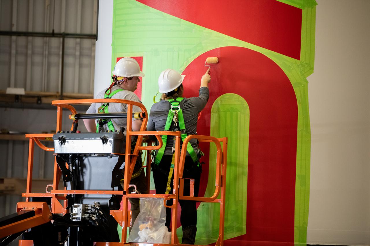 Workers with NASA’s Exploration Ground Systems (EGS) paint the bright red NASA “worm” logo on the side of an Artemis II solid rocket booster segment inside the Rotation, Processing and Surge Facility (RPSF) at Kennedy Space Center in Florida on Tuesday, Jan. 30, 2024. The EGS team used a laser projector to mask off the logo with tape, then painted the first coat of the iconic design. The booster segments will help propel the Space Launch System (SLS) rocket on the Artemis II mission to send four astronauts around the Moon as part of the agency’s effort to establish a long-term science and exploration presence at the Moon, and eventually Mars.