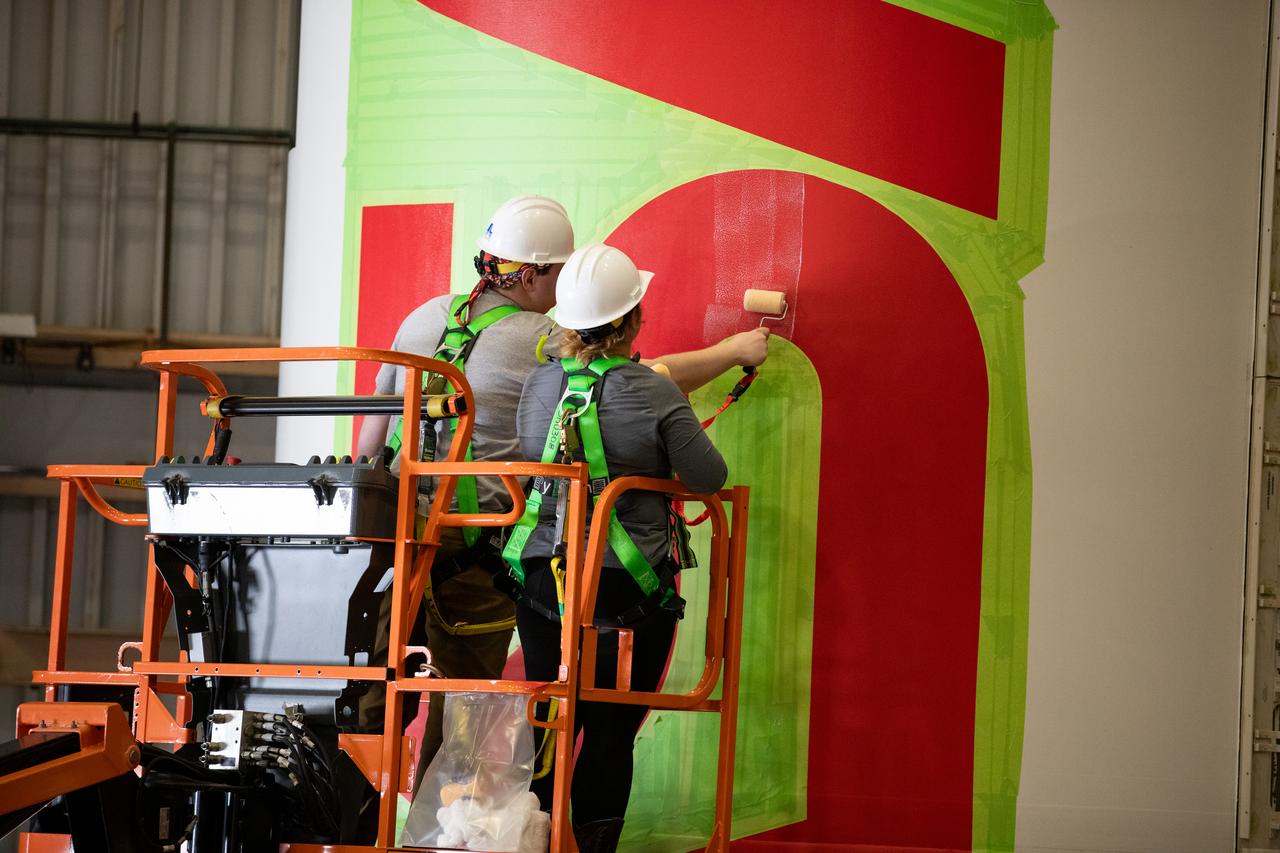 Workers with NASA’s Exploration Ground Systems (EGS) paint the bright red NASA “worm” logo on the side of an Artemis II solid rocket booster segment inside the Rotation, Processing and Surge Facility (RPSF) at Kennedy Space Center in Florida on Tuesday, Jan. 30, 2024. The EGS team used a laser projector to mask off the logo with tape, then painted the first coat of the iconic design. The booster segments will help propel the Space Launch System (SLS) rocket on the Artemis II mission to send four astronauts around the Moon as part of the agency’s effort to establish a long-term science and exploration presence at the Moon, and eventually Mars.