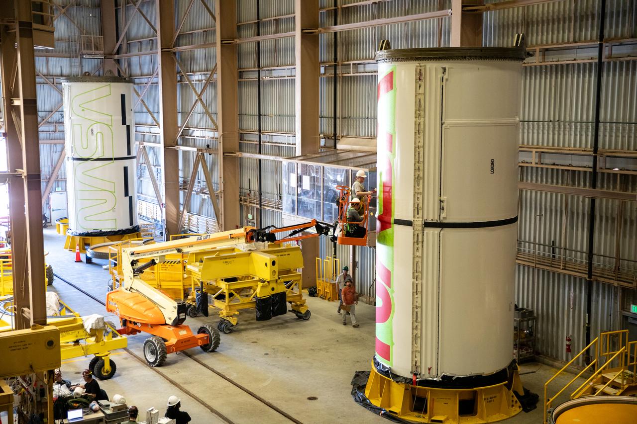 Workers with NASA’s Exploration Ground Systems (EGS) paint the bright red NASA “worm” logo on the side of an Artemis II solid rocket booster segment inside the Rotation, Processing and Surge Facility (RPSF) at Kennedy Space Center in Florida on Tuesday, Jan. 30, 2024. The EGS team used a laser projector to mask off the logo with tape, then painted the first coat of the iconic design. The booster segments will help propel the Space Launch System (SLS) rocket on the Artemis II mission to send four astronauts around the Moon as part of the agency’s effort to establish a long-term science and exploration presence at the Moon, and eventually Mars.