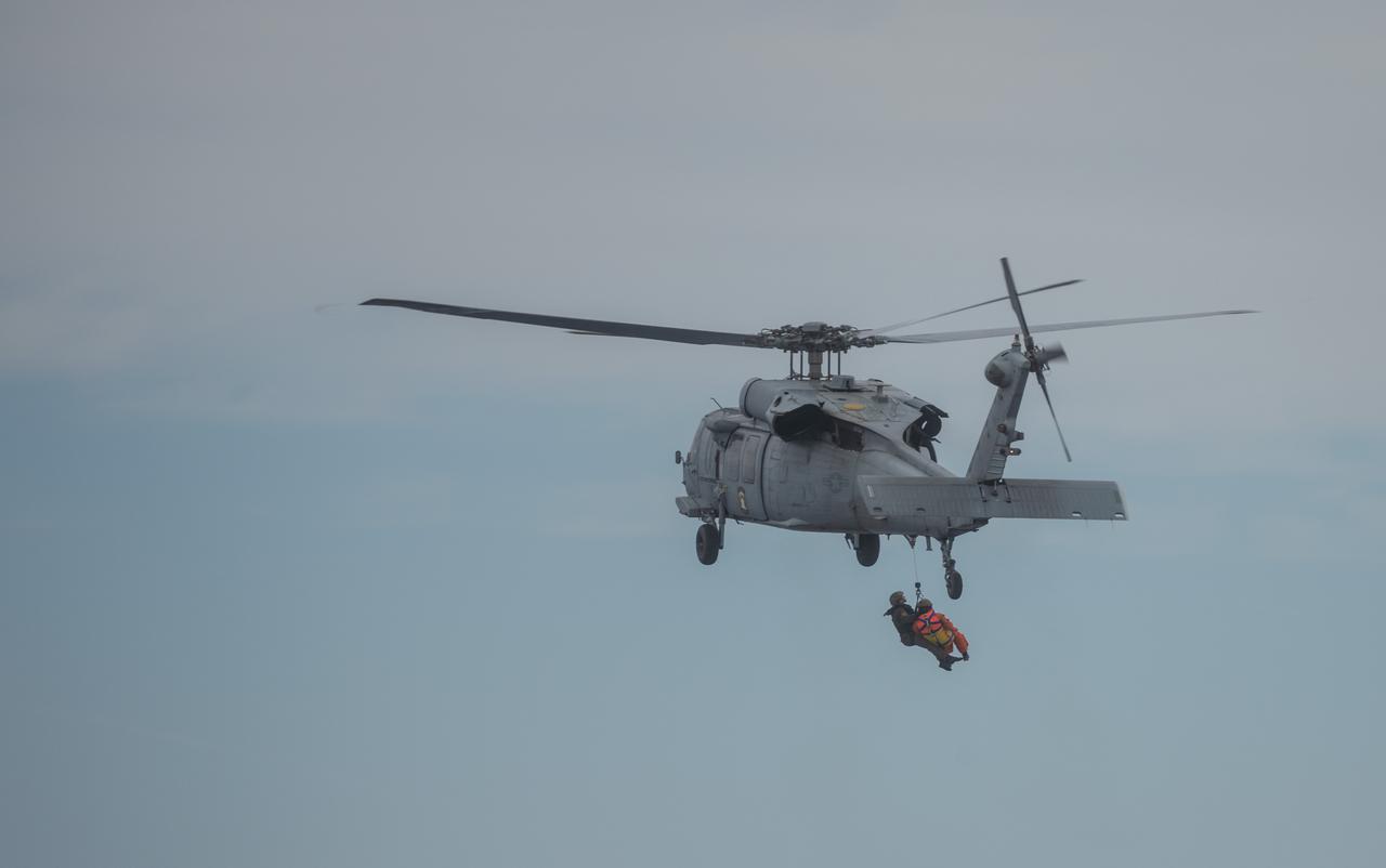 During Underway Recovery Test 11 (URT-11), conducted by NASA’s Exploration Ground System’s Landing and Recovery team and partners from the Department of Defense aboard the USS San Diego, Naval helicopter pilots from Helicopter Sea Combat Squadron (HSC) 23 “Wildcards” lift Artemis II crew members in a basket from an inflatable “front porch” that allows astronauts to be recovered out of a mockup of the Orion spacecraft off the coast of San Diego, California on Sunday, Feb. 25, 2024. URT-11 is the eleventh in a series of Artemis recovery tests, and the first time NASA and its partners put their Artemis II recovery procedures to the test with the astronauts.
