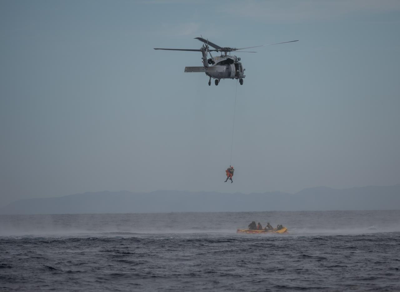 During Underway Recovery Test 11 (URT-11), conducted by NASA’s Exploration Ground System’s Landing and Recovery team and partners from the Department of Defense aboard the USS San Diego, Naval helicopter pilots from Helicopter Sea Combat Squadron (HSC) 23 “Wildcards” lift Artemis II crew members in a basket from an inflatable “front porch” that allows astronauts to be recovered out of a mockup of the Orion spacecraft off the coast of San Diego, California on Sunday, Feb. 25, 2024. URT-11 is the eleventh in a series of Artemis recovery tests, and the first time NASA and its partners put their Artemis II recovery procedures to the test with the astronauts.