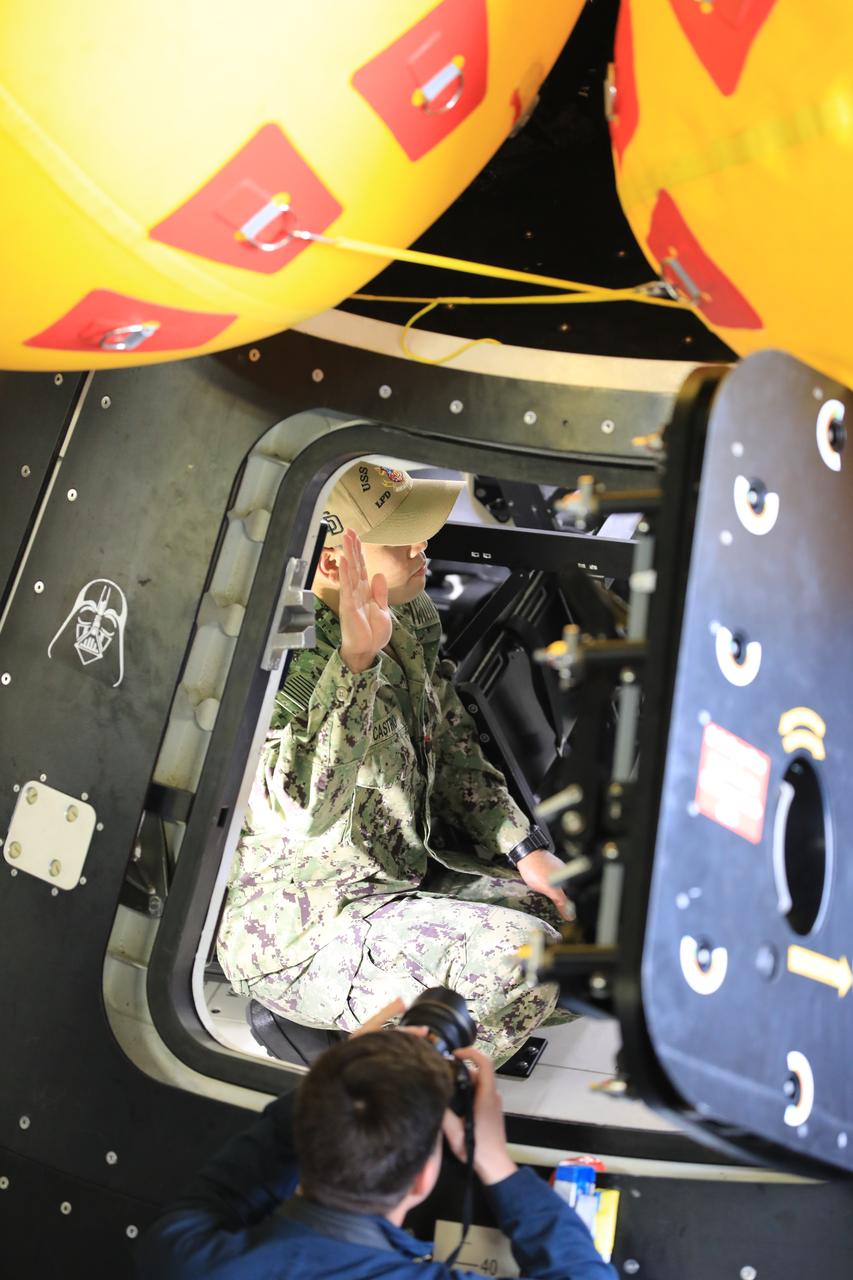 A member of the USS San Diego raises their right hand inside a mockup of the Orion spacecraft during Underway Recovery Test 11 (URT-11) aboard the USS San Diego on Monday, Feb. 26, 2024. URT-11 is the eleventh in a series of Artemis recovery tests, and the first time NASA and its partners put their Artemis II recovery procedures to the test with the astronauts. 