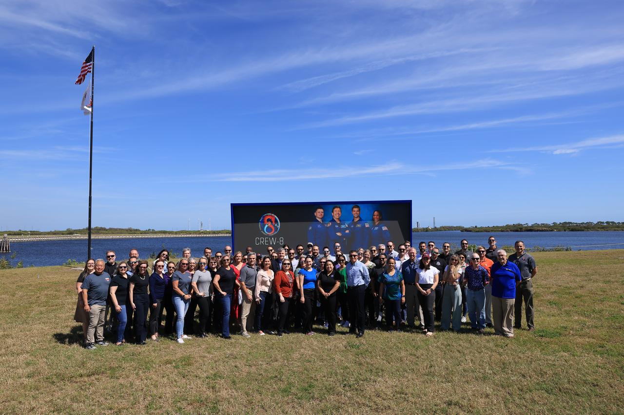 NASA Commercial Crew Program employees are photographed in front of the iconic countdown clock near the NASA News Center at the agency’s Kennedy Space Center in Florida with the Crew-8 flag raised in the background on Wednesday, Feb. 28, 2024. NASA’s SpaceX Crew-8 mission will carry NASA astronauts Matthew Dominick, Michael Barratt, and Jeanette Epps, and Roscosmos cosmonaut Alexander Grebenkin, to the International Space Station with liftoff of SpaceX’s Falcon 9 rocket and Dragon spacecraft from Kennedy’s Launch Complex 39A no earlier than 12:04 a.m. EST on Friday, March 1.