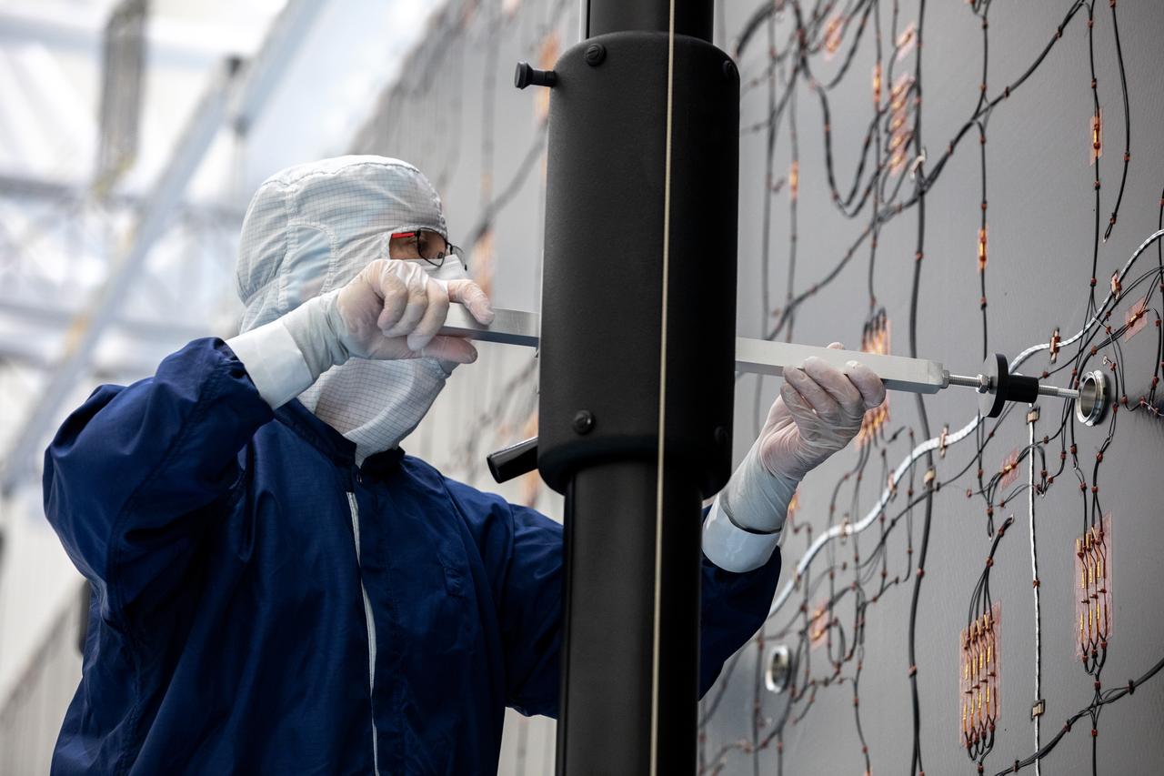 Technicians examine the first of two fully extended five-panel solar arrays built for NASA’s Europa Clipper suspended on a support system called a gravity offload fixture during inspection and cleaning as part of assembly, test, and launch operations inside the Payload Hazardous Servicing Facility at the agency’s Kennedy Space Center in Florida on Wednesday, March 6, 2024. Another name for the gravity offload fixture is the Transportable Large Envelope Deployment Facility (T-LEDF). When both solar arrays are installed and deployed on Europa Clipper – the agency’s largest spacecraft ever developed for a planetary mission – the spacecraft will span a total length of more than 100 feet and weigh 7,145 pounds without the inclusion of propellants.     