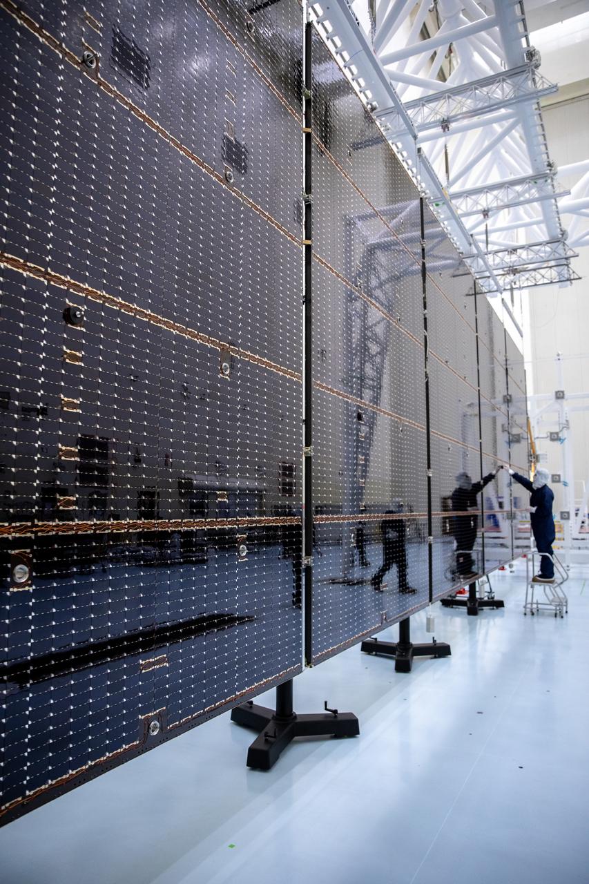 Technicians examine the first of two fully extended five-panel solar arrays built for NASA’s Europa Clipper suspended on a support system called a gravity offload fixture during inspection and cleaning as part of assembly, test, and launch operations inside the Payload Hazardous Servicing Facility at the agency’s Kennedy Space Center in Florida on Wednesday, March 6, 2024. Another name for the gravity offload fixture is the Transportable Large Envelope Deployment Facility (T-LEDF). When both solar arrays are installed and deployed on Europa Clipper – the agency’s largest spacecraft ever developed for a planetary mission – the spacecraft will span a total length of more than 100 feet and weigh 7,145 pounds without the inclusion of propellants.     