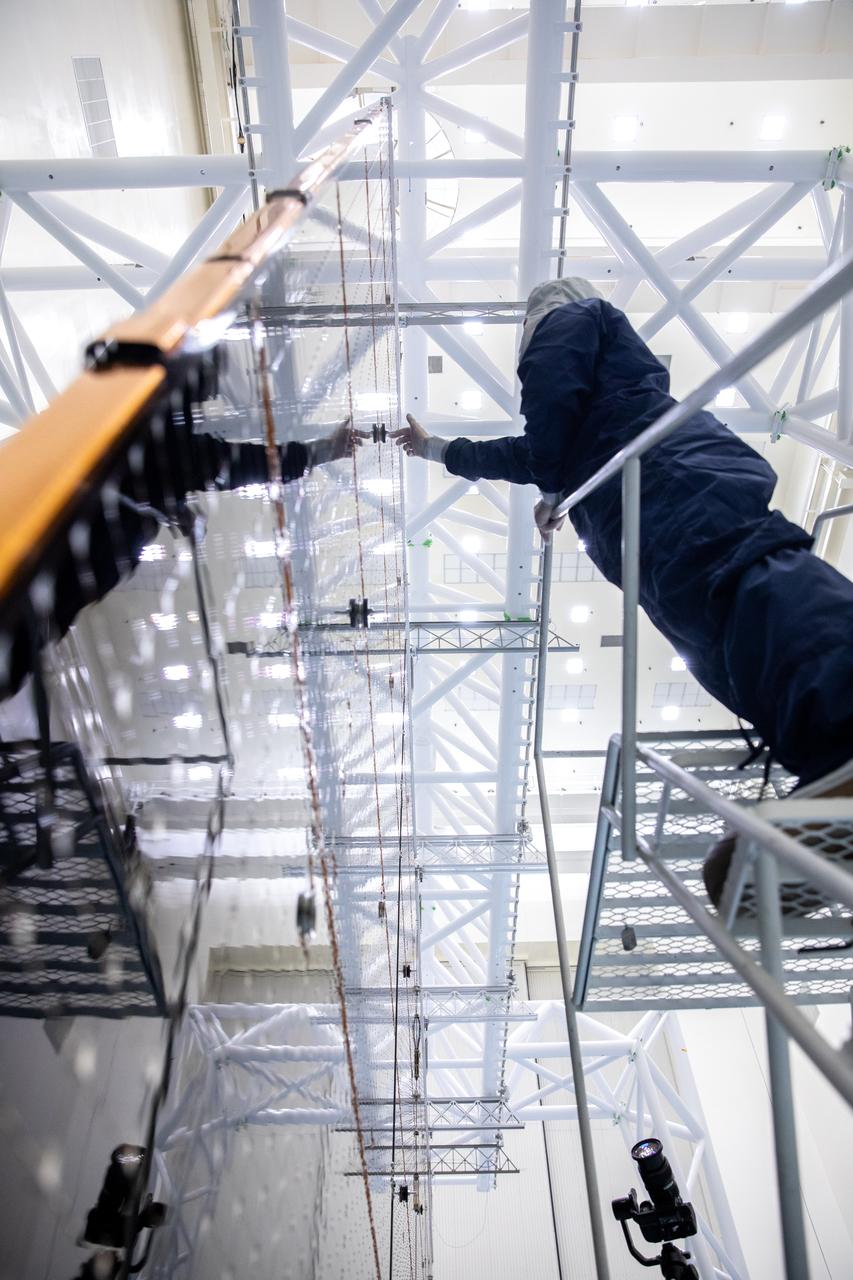 Technicians examine the first of two fully extended five-panel solar arrays built for NASA’s Europa Clipper suspended on a support system called a gravity offload fixture during inspection and cleaning as part of assembly, test, and launch operations inside the Payload Hazardous Servicing Facility at the agency’s Kennedy Space Center in Florida on Wednesday, March 6, 2024. Another name for the gravity offload fixture is the Transportable Large Envelope Deployment Facility (T-LEDF). When both solar arrays are installed and deployed on Europa Clipper – the agency’s largest spacecraft ever developed for a planetary mission – the spacecraft will span a total length of more than 100 feet and weigh 7,145 pounds without the inclusion of propellants.     
