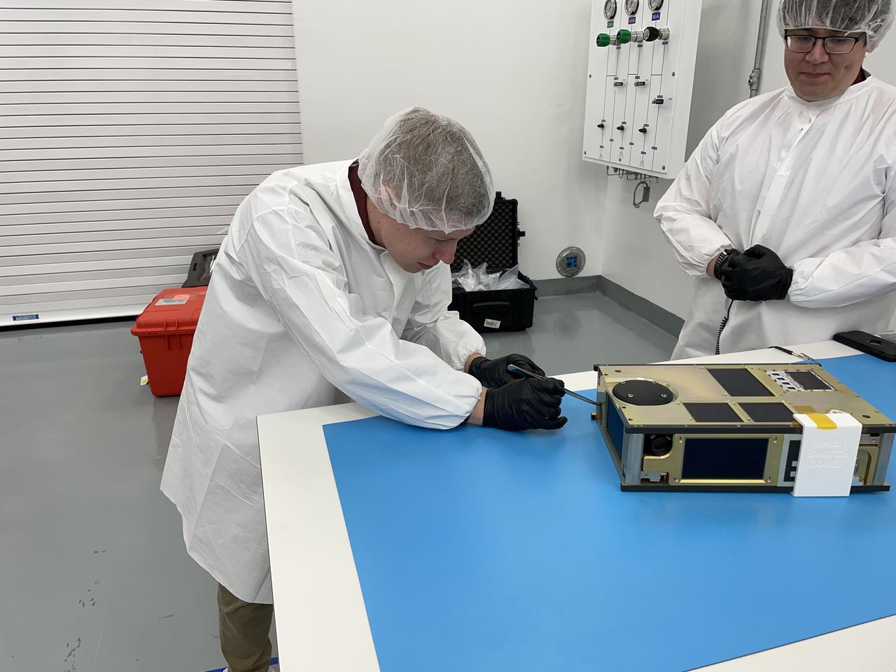 From left, NASA engineer James Berck removes the foreign object debris (FOD) cover from the relative navigation camera on the agency’s CubeSat R5 Spacecraft 4 (R5-S4) while NASA engineer Jacob Nunez-Kearny observes, at Firefly Aerospace’s Payload Processing Facility at Vandenberg Space Force Base, California on Wednesday, April 24, 2024. The spacecraft will soon be integrated for launch aboard the company’s Alpha rocket, as part of launch services provided for NASA's CubeSat Launch Initiative and Educational Launch of Nanosatellites 43 mission in support of the agency ’s Venture-Class Launch Services Demonstration 2 contract.