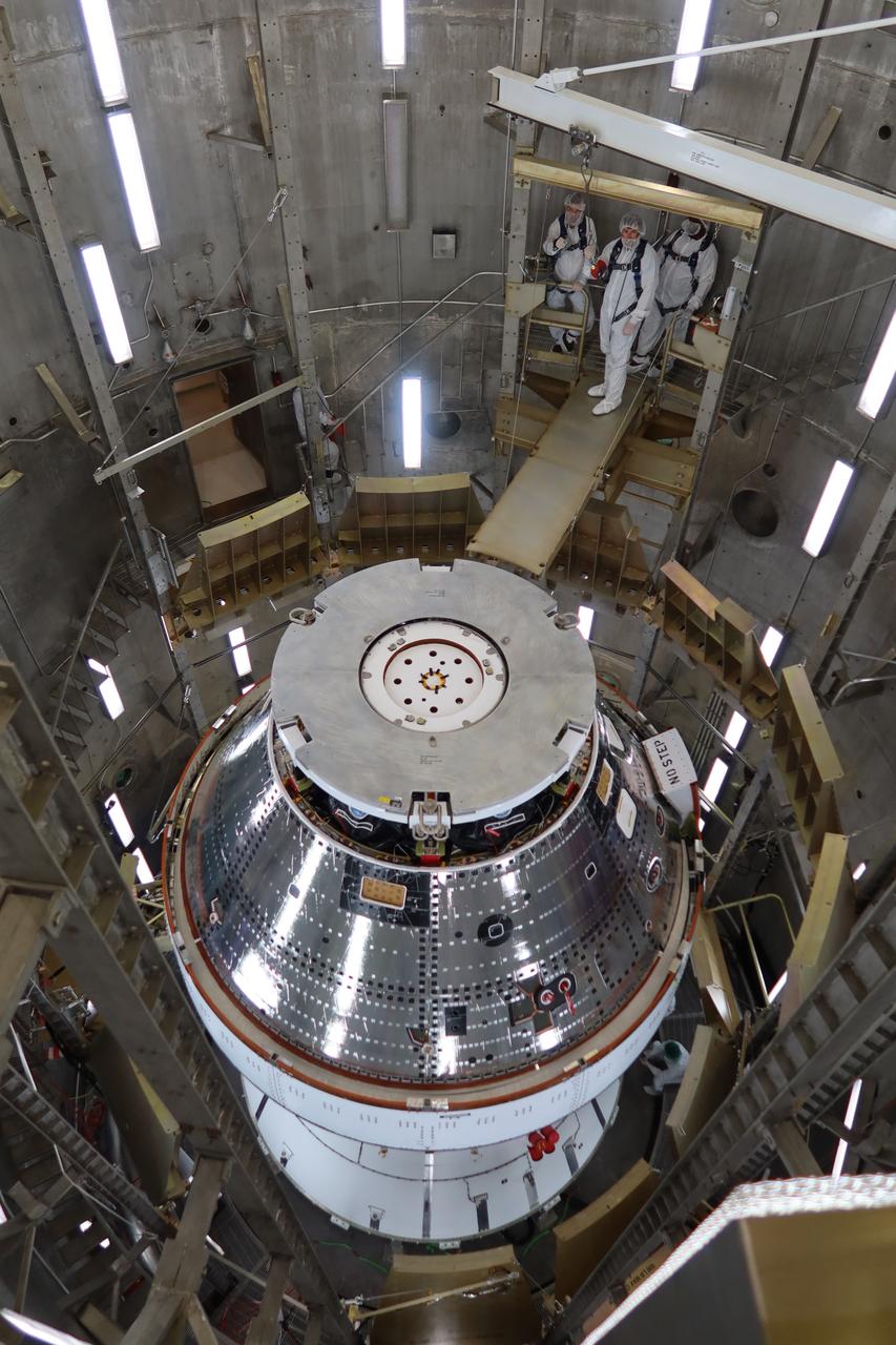 A team wearing bunny suits inside the Operations and Checkout Building at NASA's Kennedy Space Center in Florida on Saturday, April 27, 2024 prepare the Artemis II Orion spacecraft to be lifted by a 30 ton crane out of a vacuum chamber following a series of electromagnetic compatibility and interference testing. 