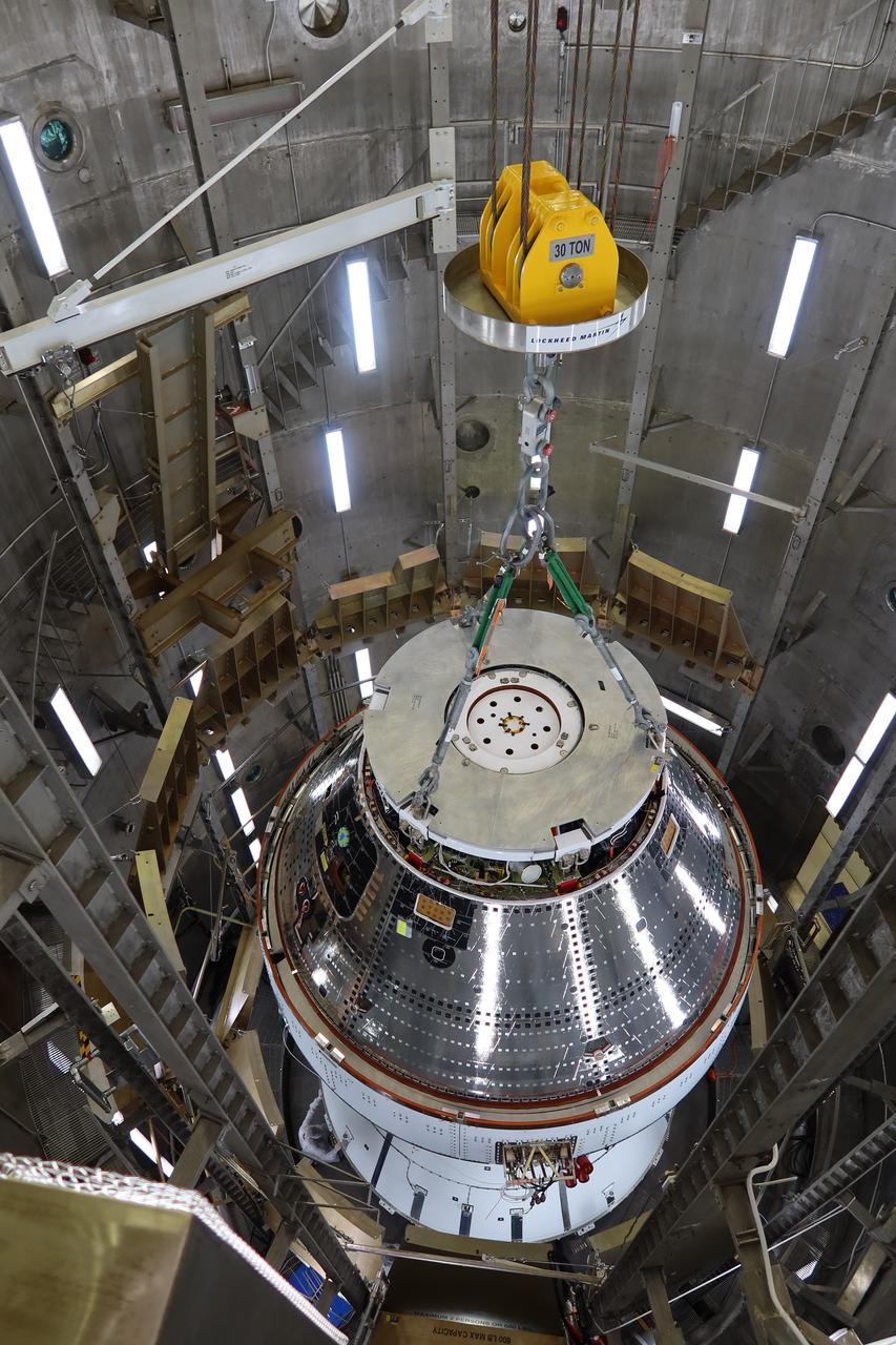 A team wearing bunny suits inside the Operations and Checkout Building at NASA's Kennedy Space Center in Florida on Saturday, April 27, 2024 prepare the Artemis II Orion spacecraft to be lifted by a 30 ton crane out of a vacuum chamber following a series of electromagnetic compatibility and interference testing. 