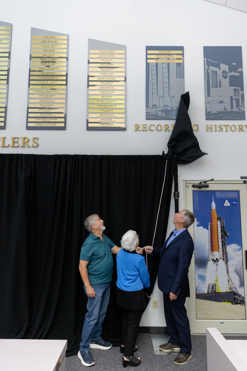 Mike Brown, Maggie Persinger, and Dan Billow were honored May 15, 2024, during the 2024 Kennedy Chroniclers ceremony at the Press Site at NASA’s Kennedy Space Center in Florida. Three brass plates bearing their names were added to the wall of the “bull pen,” where reporters traditionally gather to cover launches and events at NASA Kennedy. The three were honored for their efforts in helping tell the story of America’s space program, primarily from the Florida spaceport. They were nominated by their peers and selected by a panel of NASA officials and current space reporters.