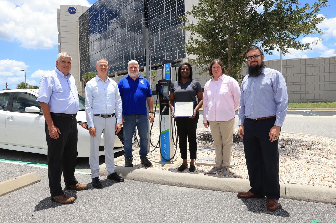 Six of the seven members of the NASA Kennedy Space Center team recognized by the White House on Tuesday, June 25, 2024, during the Presidential Federal Sustainability Awards stand next to an electric vehicle (EV) charging station in front of Kennedy's Central Campus Headquarters Building. Those members are, from left to right, center services division chief Gustavo Diaz, partnership development office chief Matthew Jimenez, then branch chief Gerald “Jay” Green, sustainability lead Lashanda Battle, transportation officer Melissa Coleman, and then transportation specialist Spencer Davis. This EV station is one of 28 installed on center through a partnership with local utility provider Florida Power & Light, allowing up to 56 electric vehicles to be charged at the same time. An additional 31 EV stations are planned at Kennedy by fall 2024, increasing the center's vehicle charging capacity by up to 118 vehicles simultaneously once they're operational.