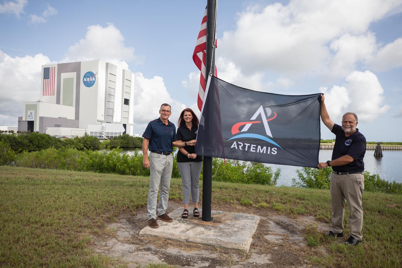 From left to right, Cliff Lanham, senior vehicle operations manager, Exploration Ground Systems; Charlie Blackwell-Thompson, Artemis launch director, Exploration Ground Systems; and Shawn Quinn, manager, Exploration Ground Systems, prepare to raise the Artemis flag near the countdown clock at NASA’s Kennedy Space Center in Florida on Monday, July 22, 2024. The flag raising marks the arrival of NASA’s massive SLS (Space Launch System) core stage via the agency’s Pegasus barge from NASA’s Michoud Assembly Facility in New Orleans. The core stage will help power SLS when it launches four astronauts around the Moon for the first crewed flight of SLS and the Orion spacecraft during the Artemis II test flight.