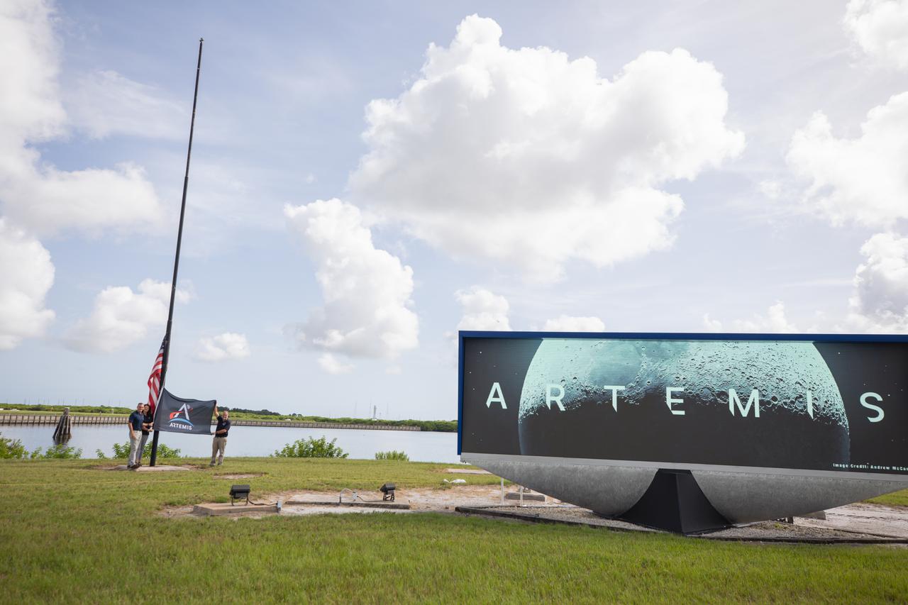 From left to right, Cliff Lanham, senior vehicle operations manager, Exploration Ground Systems; Charlie Blackwell-Thompson, Artemis launch director, Exploration Ground Systems; and Shawn Quinn, manager, Exploration Ground Systems, prepare to raise the Artemis flag near the countdown clock at NASA’s Kennedy Space Center in Florida on Monday, July 22, 2024. The flag raising marks the arrival of NASA’s massive SLS (Space Launch System) core stage via the agency’s Pegasus barge from NASA’s Michoud Assembly Facility in New Orleans. The core stage will help power SLS when it launches four astronauts around the Moon for the first crewed flight of SLS and the Orion spacecraft during the Artemis II test flight.