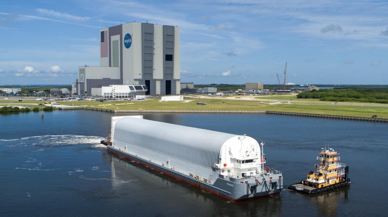 In this aerial view, NASA’s Pegasus barge, carrying the agency’s massive SLS (Space Launch System) core stage, arrives at NASA’s Kennedy Space Center Complex 39 turn basin wharf in Florida on Tuesday, July 23, 2024, after journeying from the agency’s Michoud Assembly Facility in New Orleans. The core stage is the next piece of Artemis hardware to arrive at the spaceport and will be offloaded and moved to NASA Kennedy’s Vehicle Assembly Building, where it will be prepared for integration ahead of the Artemis II launch.