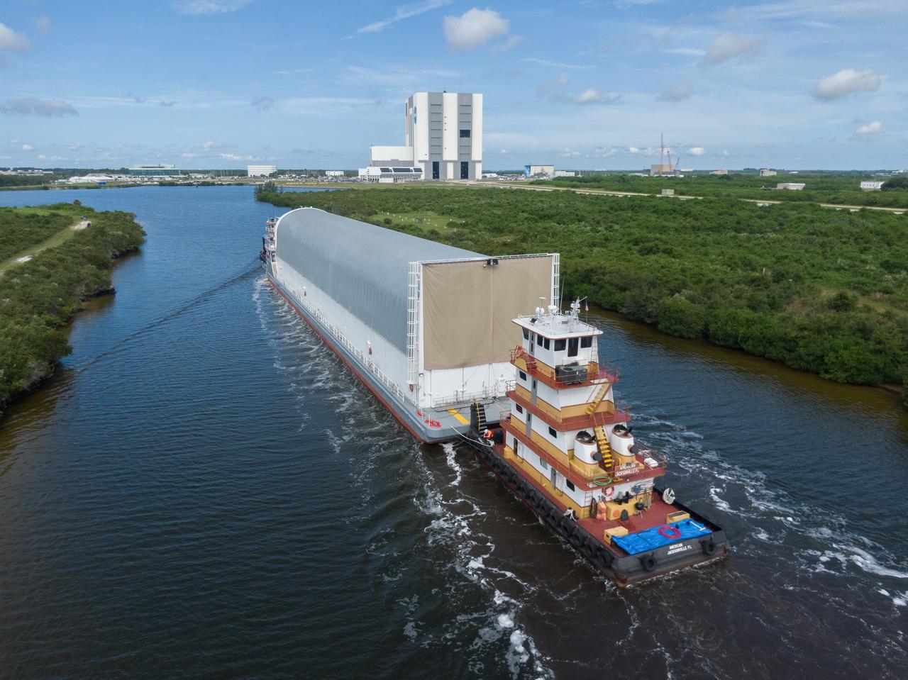In this aerial view, NASA’s Pegasus barge, carrying the agency’s massive SLS (Space Launch System) core stage, arrives at NASA’s Kennedy Space Center Complex 39 turn basin wharf in Florida on Tuesday, July 23, 2024, after journeying from the agency’s Michoud Assembly Facility in New Orleans. The core stage is the next piece of Artemis hardware to arrive at the spaceport and will be offloaded and moved to NASA Kennedy’s Vehicle Assembly Building, where it will be prepared for integration ahead of the Artemis II launch.