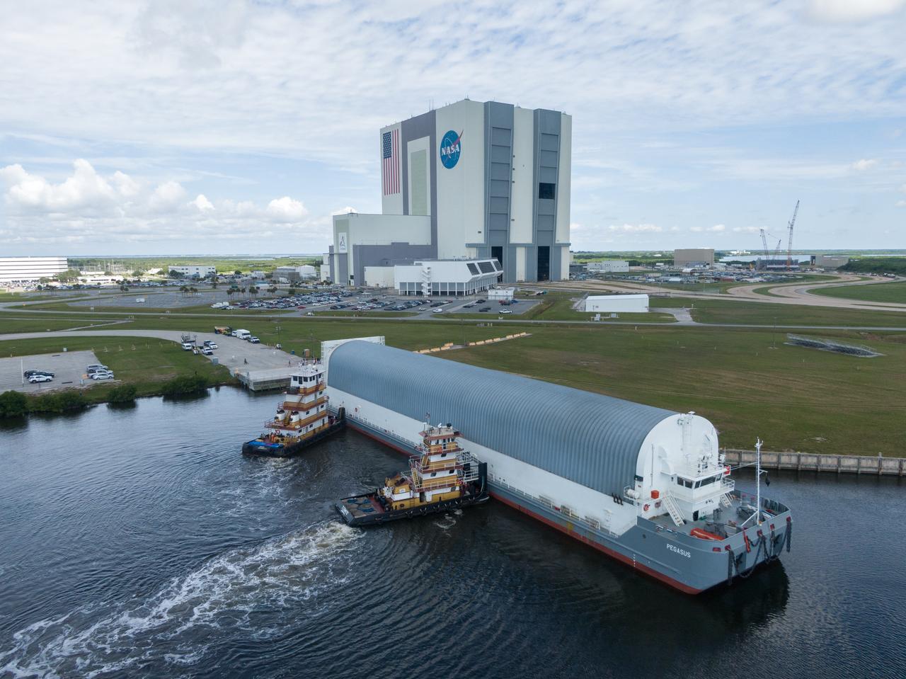 In this aerial view, NASA’s Pegasus barge, carrying the agency’s massive SLS (Space Launch System) core stage, arrives at NASA’s Kennedy Space Center Complex 39 turn basin wharf in Florida on Tuesday, July 23, 2024, after journeying from the agency’s Michoud Assembly Facility in New Orleans. The core stage is the next piece of Artemis hardware to arrive at the spaceport and will be offloaded and moved to NASA Kennedy’s Vehicle Assembly Building, where it will be prepared for integration ahead of the Artemis II launch.