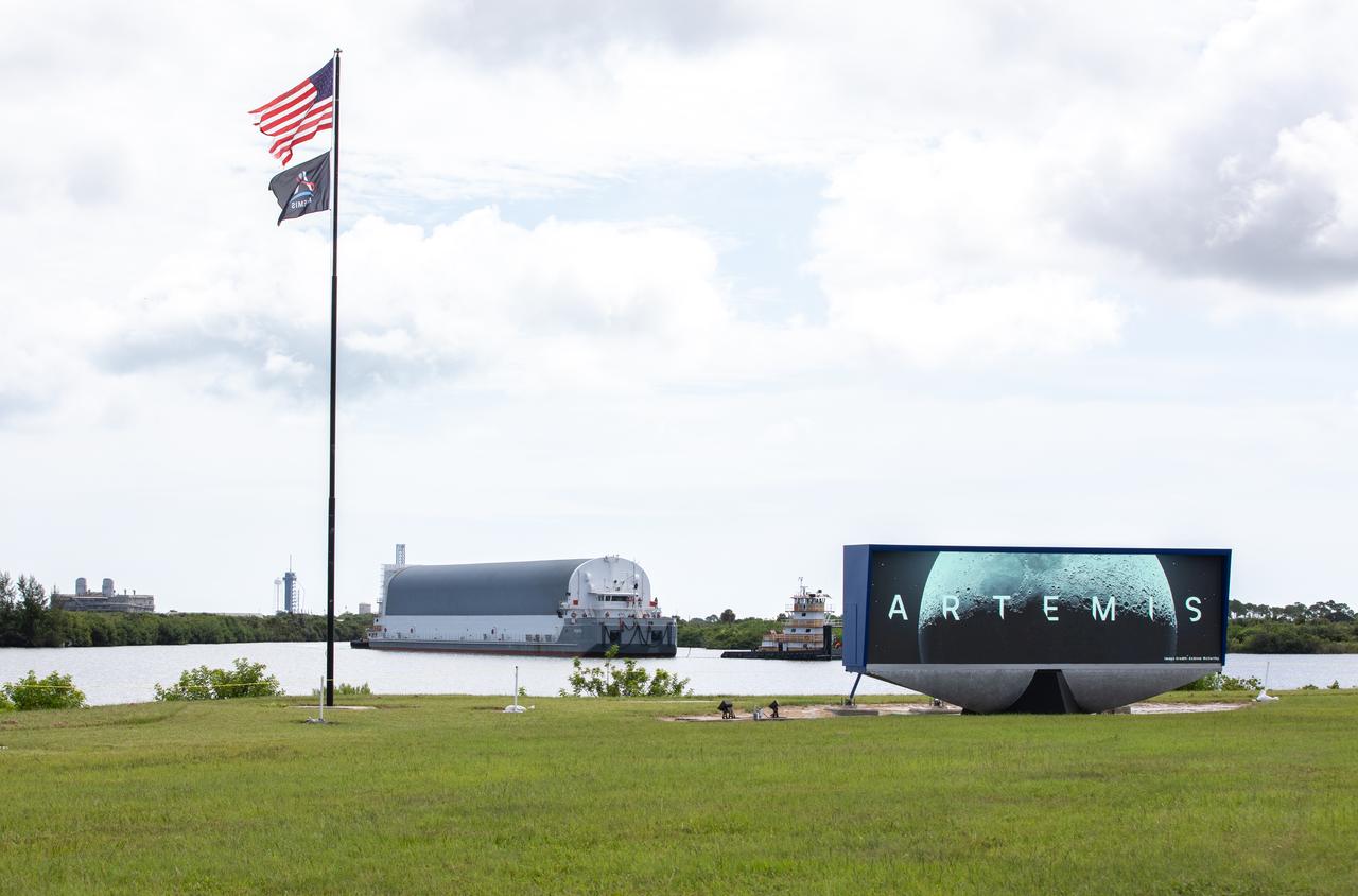 Behind the iconic countdown clock at NASA’s Kennedy Space Center in Florida, the agency’s Pegasus barge completes its 900-mile journey from NASA’s Michoud Assembly Facility in New Orleans carrying the powerful SLS (Space Launch System) core stage on Tuesday, July 23, 2024. Teams with NASA's Exploration Ground Systems (EGS) will offload the rocket stage and transfer it to the spaceport’s Vehicle Assembly Building to prepare it for integration atop the mobile launcher ahead of the Artemis II launch.