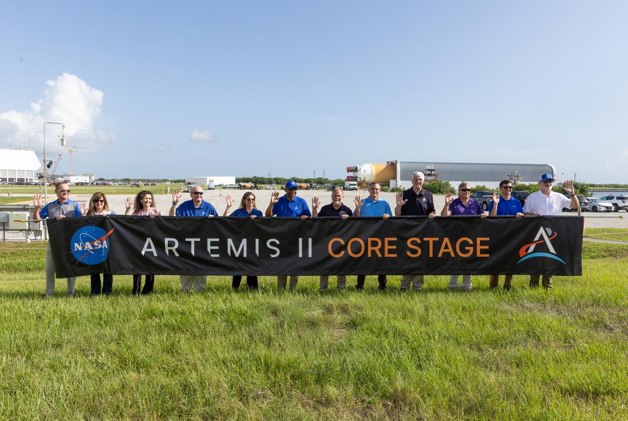 From left, John Ramsey, chief transformation officer for Jacobs; Jennifer Kunz, associate director, technical, NASA’s Kennedy Space Center; Lorna Kenna, vice president and general manager, Jacobs; Burt Summerfield, associate director, management, NASA Kennedy; Catherine Koerner, associate administrator for NASA’s Exploration Systems Development Mission Directorate; Kelvin Manning, deputy director, NASA Kennedy; Shawn Quinn, manager, NASA’s Exploration Ground Systems; Cliff Lanham, senior vehicle operations manager, NASA’s Exploration Ground Systems; Matthew Ramsey, Artemis II mission manager; Paul Hudson, Jacobs senior vehicle engineer; Jay Grow, Boeing’s associate chief engineer for Space Launch System Launch Operations; and Bill Muddle, lead RS-25 field engineer at Aerojet Rocketdyne, hold a banner to celebrate the arrival of the Artemis II SLS (Space Launch System) core stage at NASA’s Kennedy Space Center on Wednesday, July 24, 2024. Journeying from NASA’s Michoud Assembly Facility in New Orleans aboard the Pegasus barge, the core stage arrived at the Florida spaceport on July 23, 2024, to be processed for flight by NASA’s Exploration Ground Systems Program. 