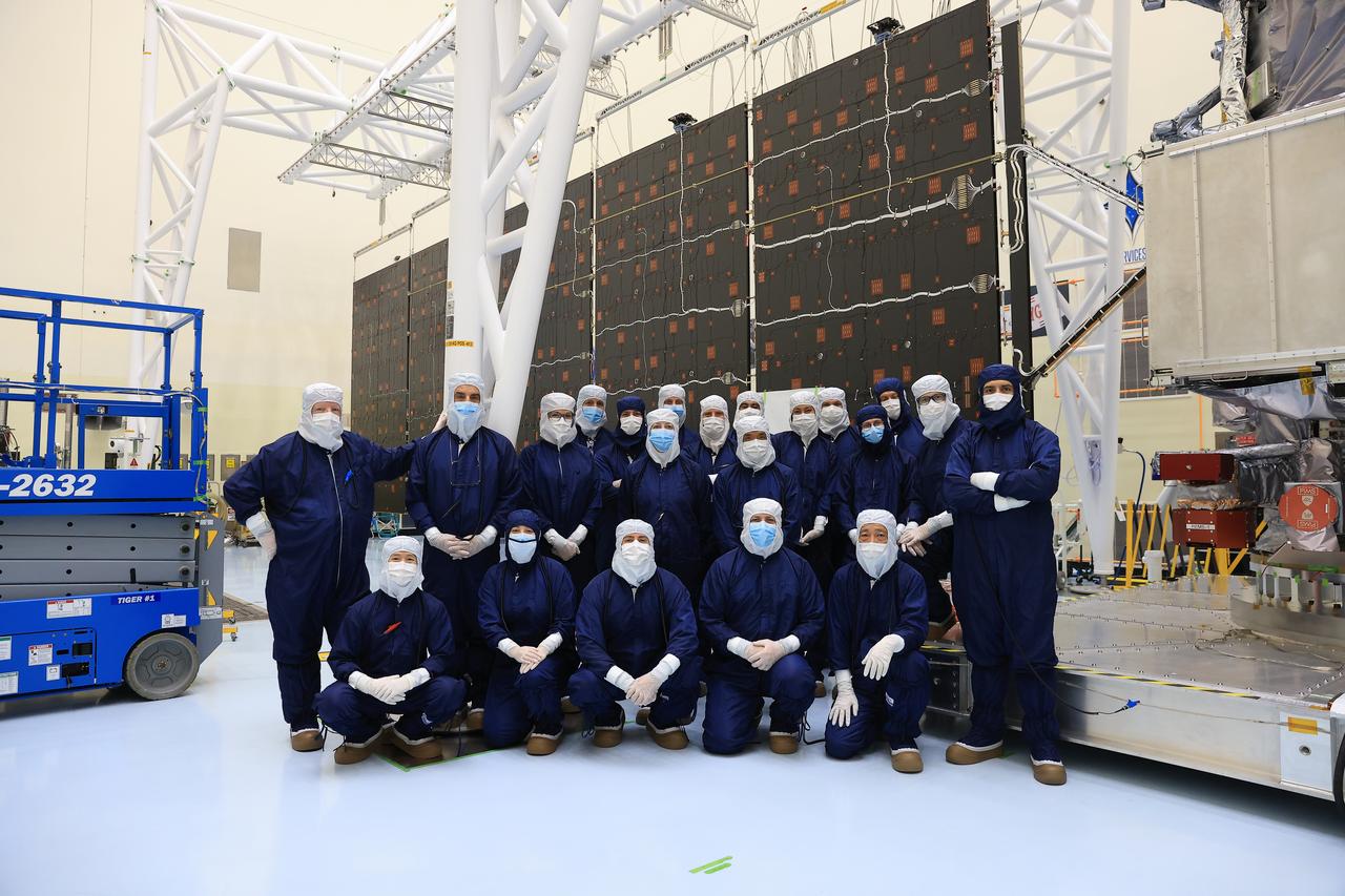 Technicians pose for a photo in front of one of the two “wings” comprising the solar arrays for NASA’s Europa Clipper spacecraft on Friday, Aug. 23, 2024, at the Payload Hazardous Servicing Facility at the agency’s Kennedy Space Center in Florida. Each array measures about 46.5 feet (14.2 meters) long and about 13.5 feet (4.1 meters) high. The spacecraft needs the massive solar arrays to power to Jupiter’s icy moon Europa to help scientists better understand the astrobiological potential for habitable worlds beyond our planet.