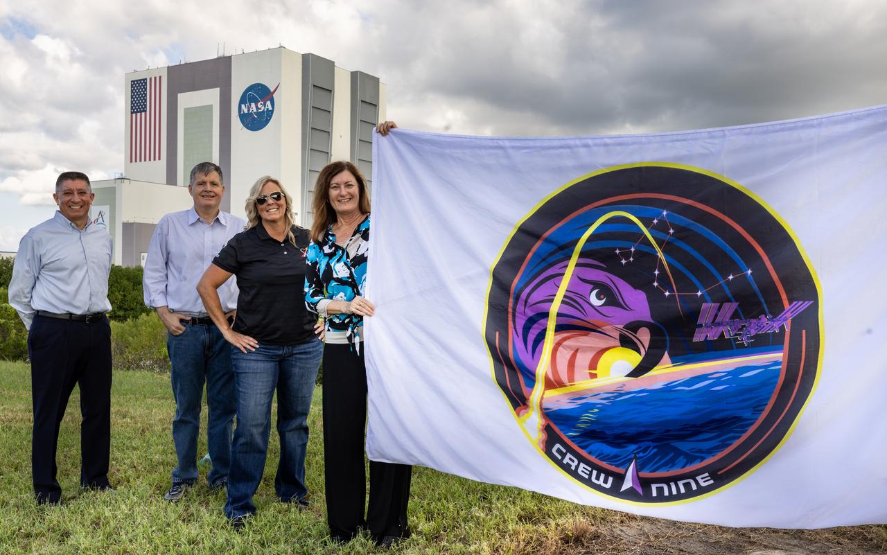 From left, Richard Jones, CCP (Commercial Crew Program) deputy program manager at NASA’s Johnson Space Center in Houston; Steve Stich, program manager for CCP; Dana Hutcherson, CCP deputy program manager at NASA’s Kennedy Space Center in Florida; and Deb Cole, CCP technical manager, pose with the agency’s SpaceX Crew-9 mission flag near the countdown clock at the NASA News Center at Kennedy on Tuesday, Sept. 24, 2024. The Crew-9 mission will send NASA astronaut Nick Hague and Roscosmos cosmonaut Aleksandr Gorbunov to the International Space Station aboard SpaceX’s Dragon spacecraft and Falcon 9 rocket.