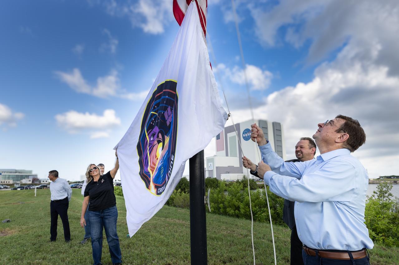David Forrest (right), deputy manager of the SE&I (Systems Engineering and Integration) Office in NASA’s Commercial Low Earth Orbit Development Program, with help of NASA’s CCP (Commercial Crew Program) Deputy Program Manager Dana Hutcherson and NASA Public Affairs Officer Steven Siceloff, raises the agency’s SpaceX Crew-9 mission flag near the countdown clock at the NASA News Center at the agency’s Kennedy Space Center in Florida on Tuesday, Sept. 24, 2024. Forrest previously served as deputy manager for CCP’s SE&I Office at Kennedy. In the background is CCP’s Deputy Program Manager at NASA’s Johnson Space Center in Houston Richard Jones (far left) and CCP program manager Steve Stich. The Crew-9 mission will send NASA astronaut Nick Hague and Roscosmos cosmonaut Aleksandr Gorbunov to the International Space Station aboard SpaceX’s Dragon spacecraft and Falcon 9 rocket. 