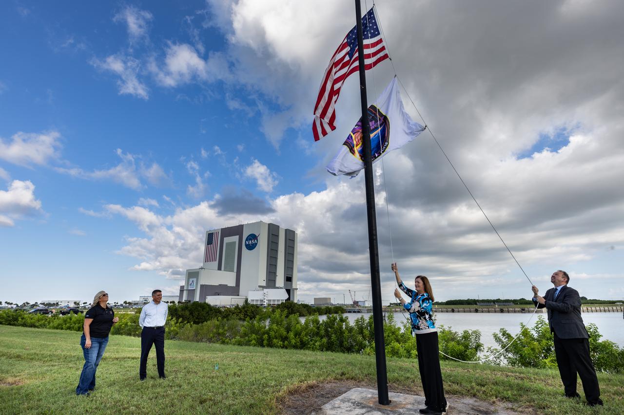 Deb Cole (second from right), CCP (Commercial Crew Program) technical manager, with help from NASA Public Affairs Officer Steven Siceloff, raises the agency’s SpaceX Crew-9 mission flag near the countdown clock at the NASA News Center at the agency’s Kennedy Space Center in Florida on Tuesday, Sept. 24, 2024. In the background looking on is CCP Deputy Program Manager Dana Hutcherson (far left) at Kennedy and CCP Deputy Program Manager at NASA’s Johnson Space Center in Houston Richard Jones. The Crew-9 mission will send NASA astronaut Nick Hague and Roscosmos cosmonaut Aleksandr Gorbunov to the International Space Station aboard SpaceX’s Dragon spacecraft and Falcon 9 rocket. 