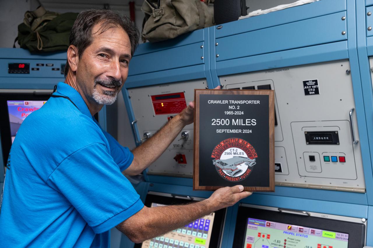 John Giles, crawler element operations manager for NASA’s Exploration Ground Systems, holds a plaque near the odometer of the agency’s crawler-transporter 2, on Wednesday, Sept. 25, 2024, at NASA’s Kennedy Space Center in Florida, commemorating the milestone of 2,500 miles traveled since its construction in 1965. Crawler-transporter 2 reached the milestone while teams took it on a trip in preparation for supporting the roll of the mobile launcher from Launch Pad 39B back into the spaceport’s Vehicle Assembly Building ahead of the Artemis II launch. Built originally to transport massive Saturn V rockets during the Apollo Program, crawler-transporter 2 continued its service during the Space Shuttle Program, and currently transports the massive SLS (Space Launch System) rocket and Orion spacecraft atop the mobile launcher as part of the agency’s Artemis campaign. 
