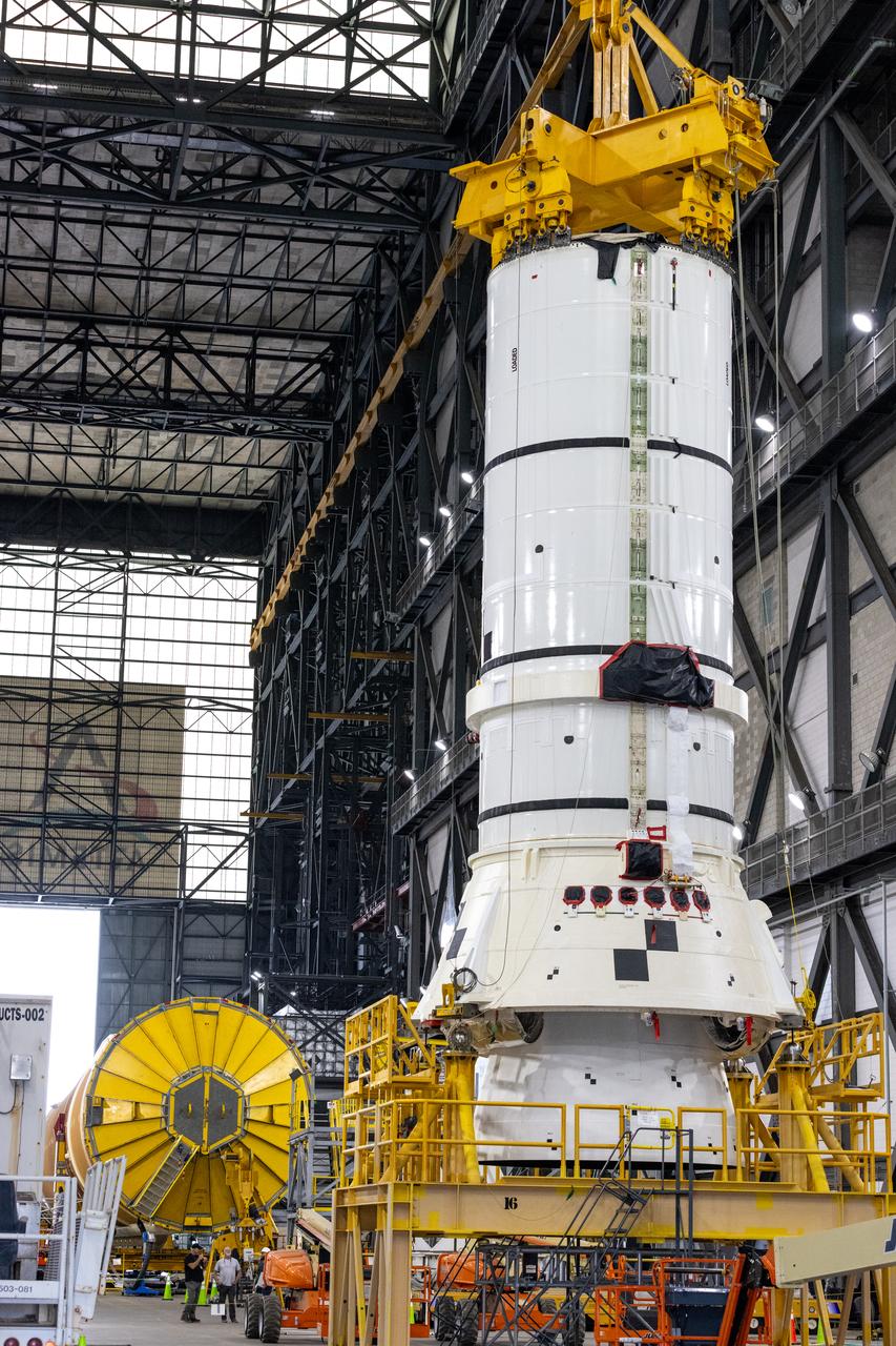 Down the transfer aisle from the Artemis II SLS (Space Launch System) core stage, engineers and technicians with the Exploration Ground Systems Program attach an overhead crane to the left aft assembly, or bottom portion of the solid rocket boosters for the SLS rocket inside the Vehicle Assembly Building at NASA’s Kennedy Space Center on Tuesday, Nov. 19, 2024. The crane will lift the aft assembly on top of the mobile launcher 1 followed by the right aft assembly and stack the remaining booster segments for the Artemis II mission.  