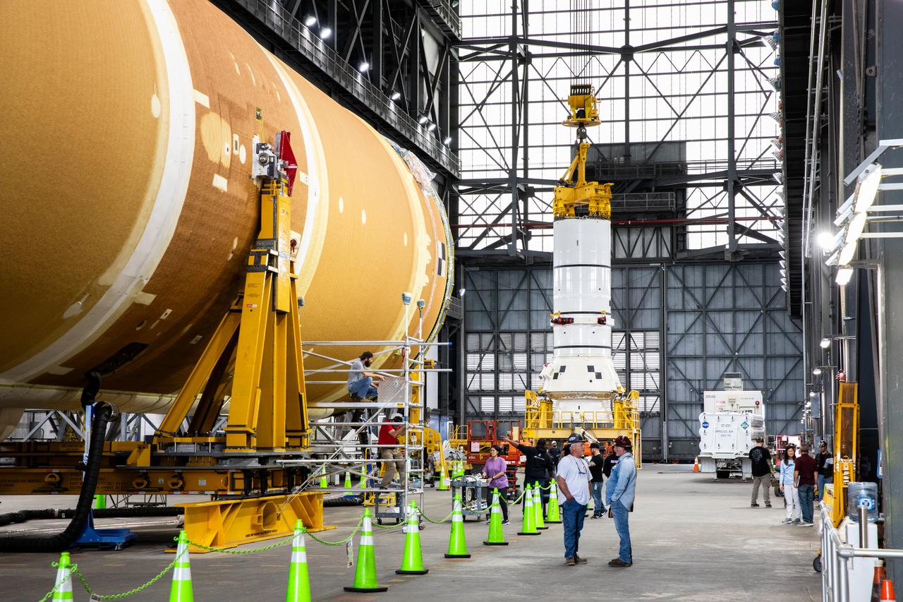 Down the transfer aisle from the Artemis II SLS (Space Launch System) core stage, engineers and technicians with the Exploration Ground Systems Program attach an overhead crane to the left aft assembly, or bottom portion of the solid rocket boosters for the SLS rocket, inside the Vehicle Assembly Building at NASA’s Kennedy Space Center on Tuesday, Nov. 19, 2024. The crane will lift the aft assembly on top of the mobile launcher 1 followed by the right aft assembly and stack the remaining booster segments for the Artemis II mission.