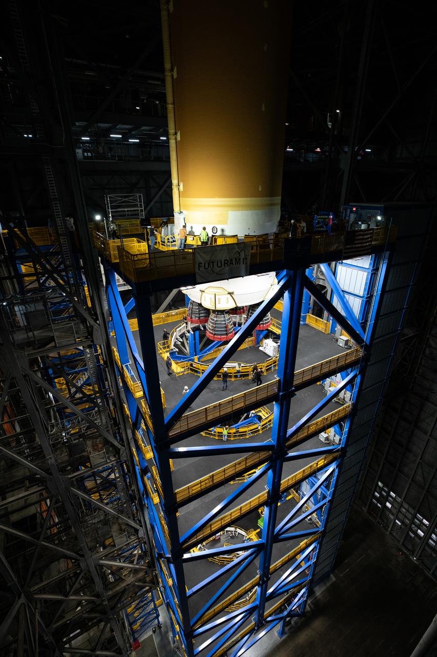 Teams with NASA’s Exploration Ground Systems transport lower the agency’s 212-foot-tall SLS (Space Launch System) core stage into High Bay 2 at the Vehicle Assembly Building at NASA’s Kennedy Space Center in Florida on Wednesday, Dec. 11, 2024. The one-of-a kind lifting beam is designed to lift the core stage from the transfer aisle to High Bay 2 where it will remain while teams stack the two solid rocket boosters on top of mobile launcher 1 for the SLS core stage. Boeing and their sub-contractor Futuramic refurbished High Bay 2 to increase efficiencies while processing core stages for Artemis II and beyond.